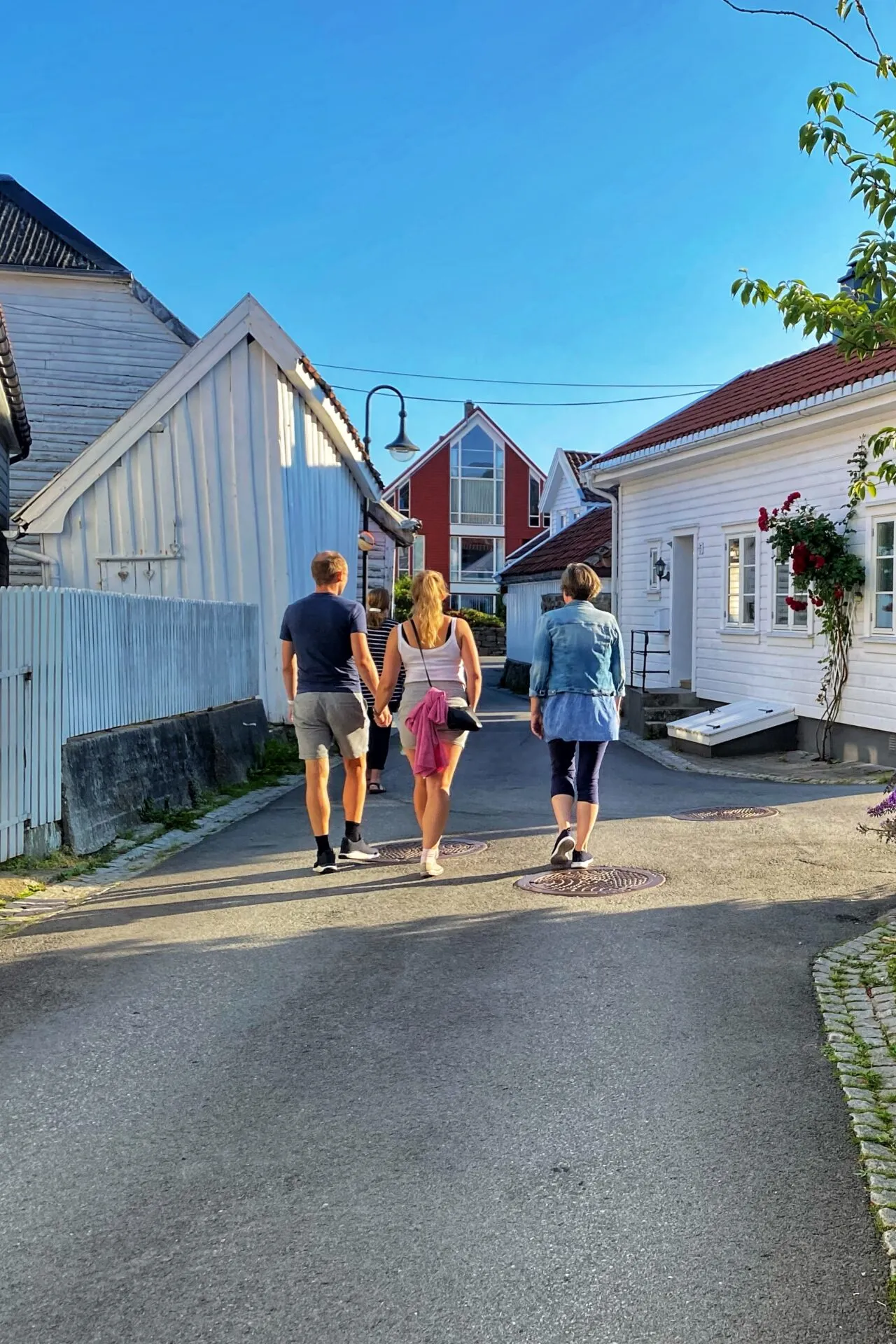 Folk spaserer gjennom en gate med hvite trehus og blomstrende sommerfuglbusk en solrik sommerdag