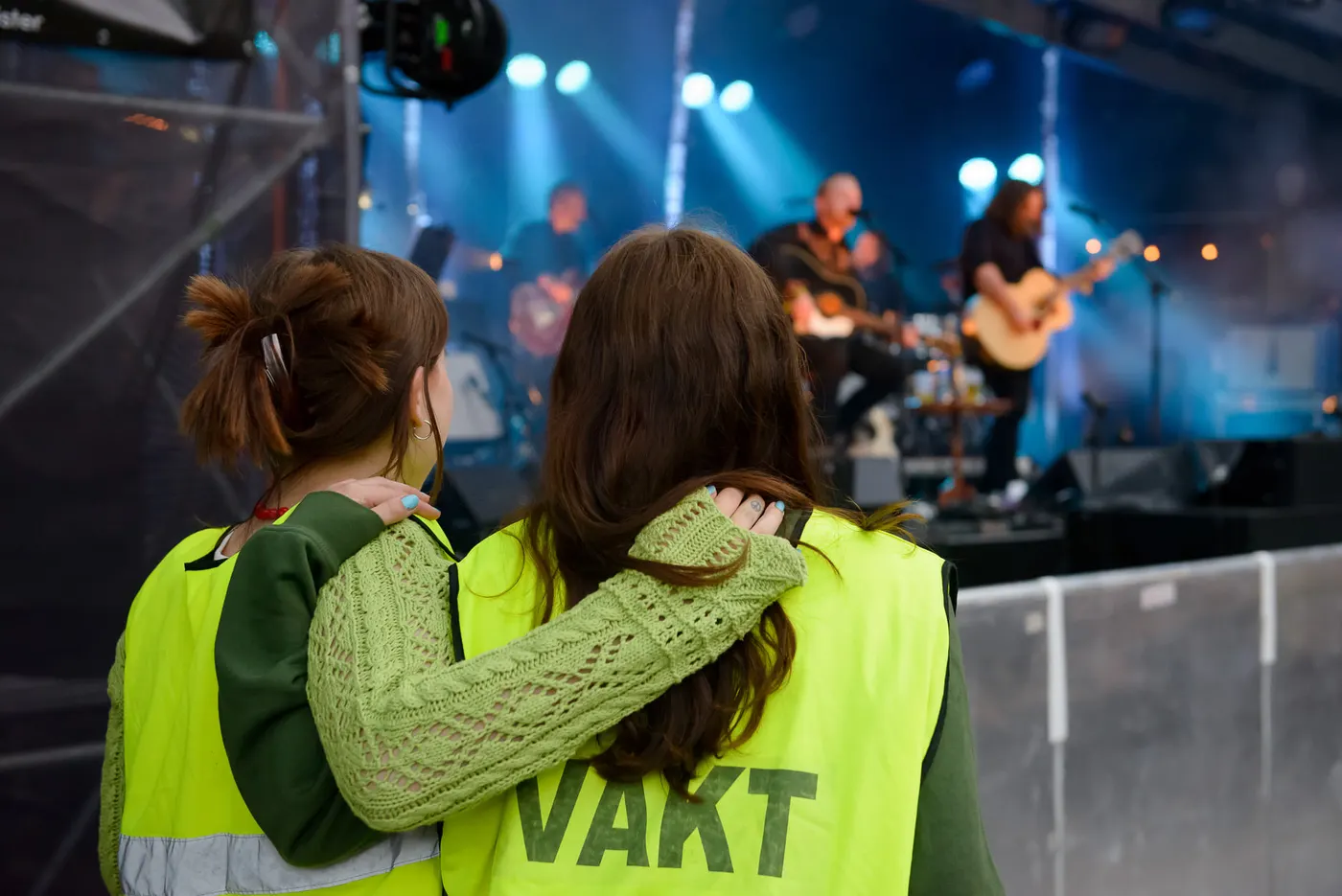 To venner med armene rundt hverandre foran en konsertscene i blått lys