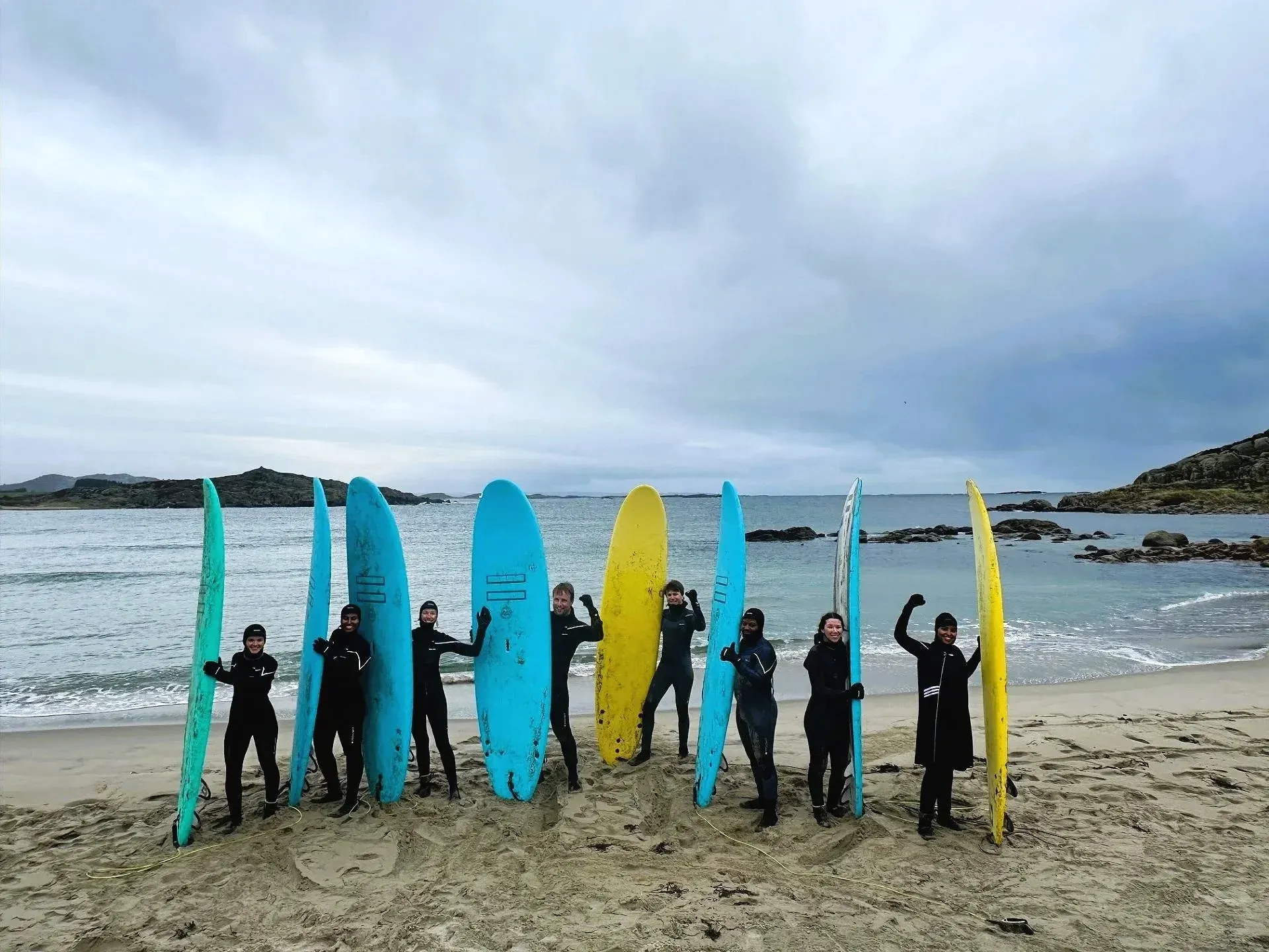 Unge i våtdrakt jubler ved siden av rekka med surfebrett på en strand på Lista