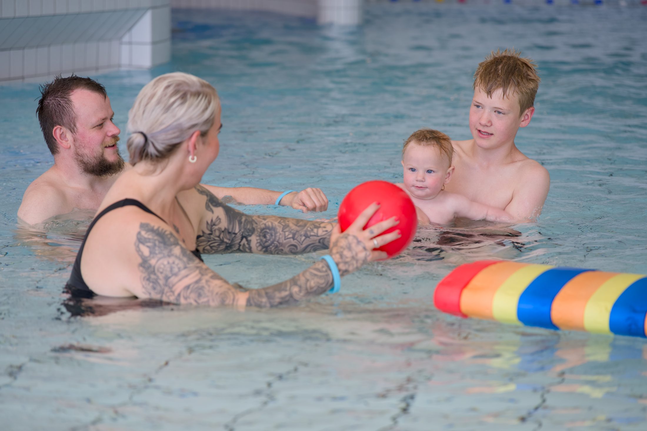 Familie som leker med ball i bassenget