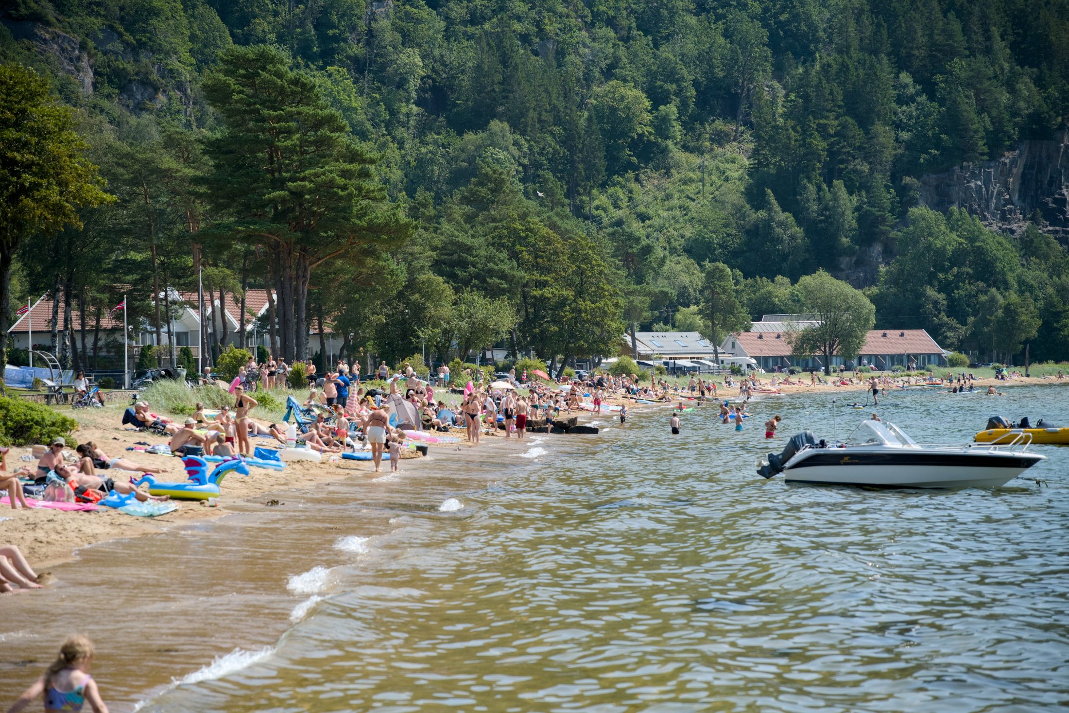 Vid sandstrand med badegjester og en båt