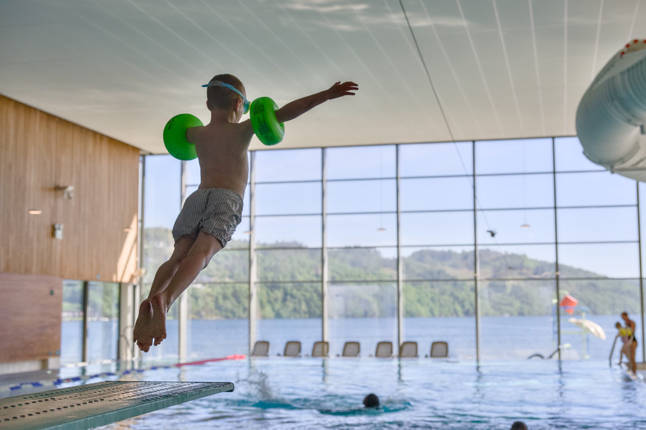 A child in mid-air above the edge of the pool in front of the panoramic window