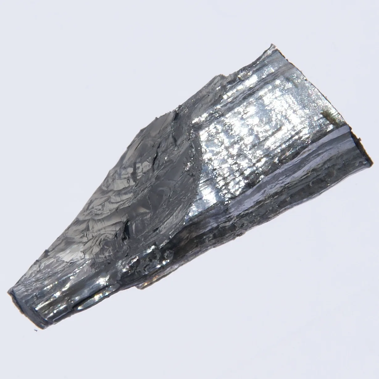 A shiny, silver-grey crystal of pure molybdenum against a light background. The surface is layered and reflective.
