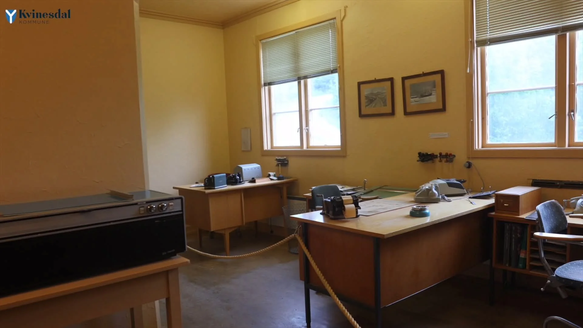 An old office with yellow walls, desks, a typewriter and a green telephone, roped off.
