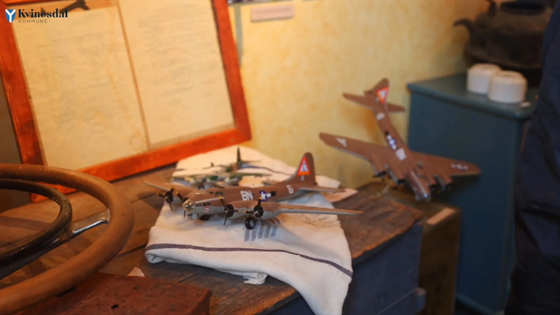 Models of two four-engined bombers on a table, beside an old steering wheel and a framed document.