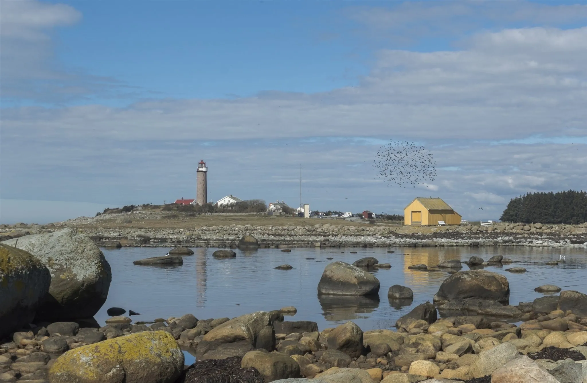 Lista fyr sett over steinene og det stille vannet i Vågsvollvika