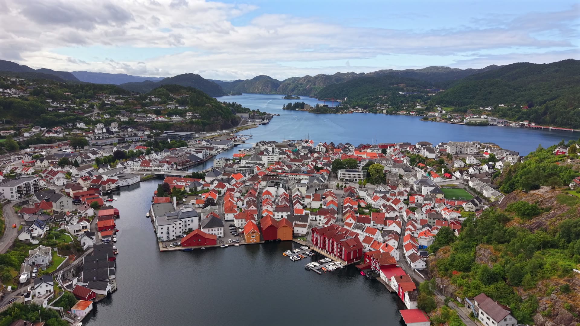 Flekkefjord sentrum fra lufta: hvite trehus rundt det indre havnebassenget, småbåtene ved kaia og heiene bak
