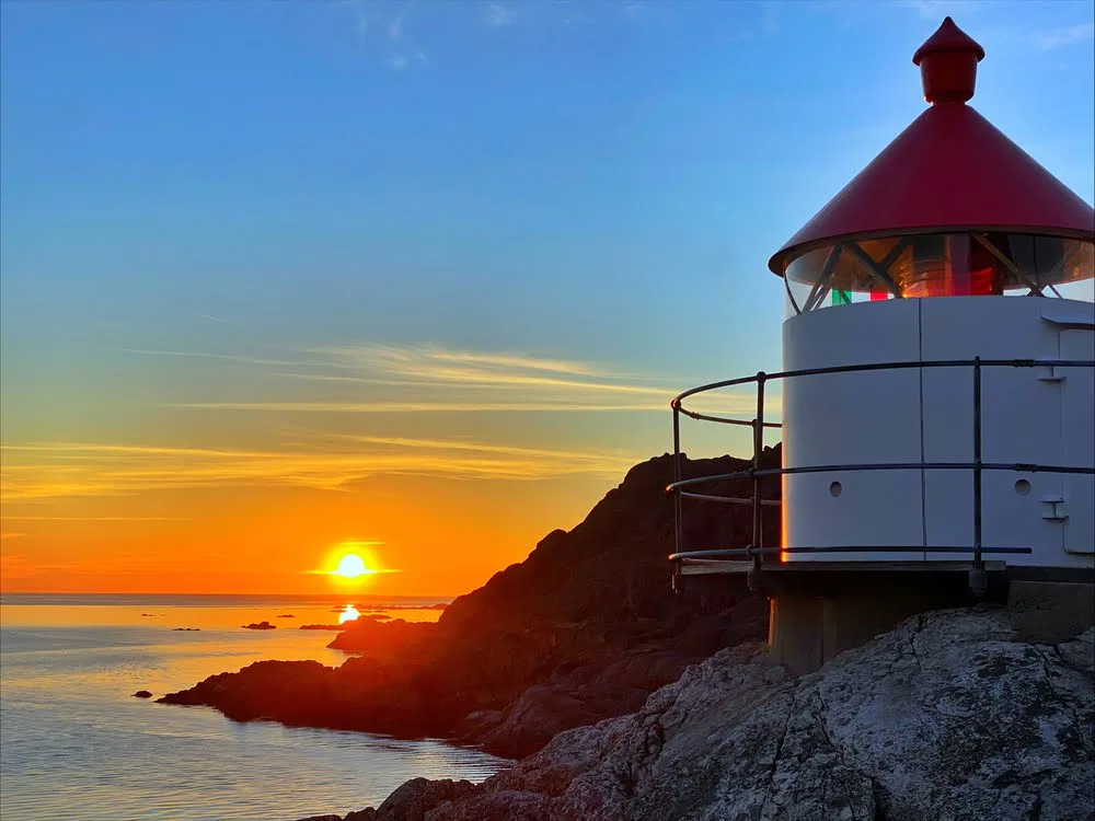 Solnedgang ved kysten utenfor Åna-Sira, med et fyr i silhuett