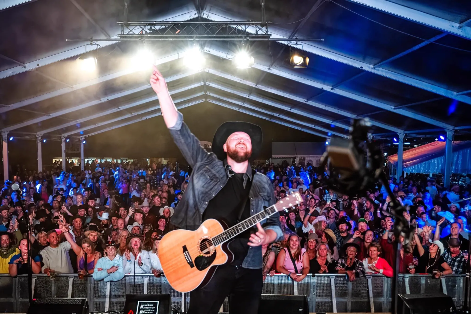 Countryartist Arthur Stulien med cowboyhatt og gitar på en scene, med armen i været foran et stort publikum