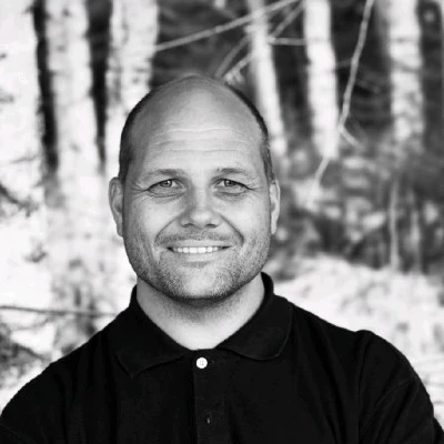 Arne Eiken, portrett i svart-hvitt foran bjørkestammer