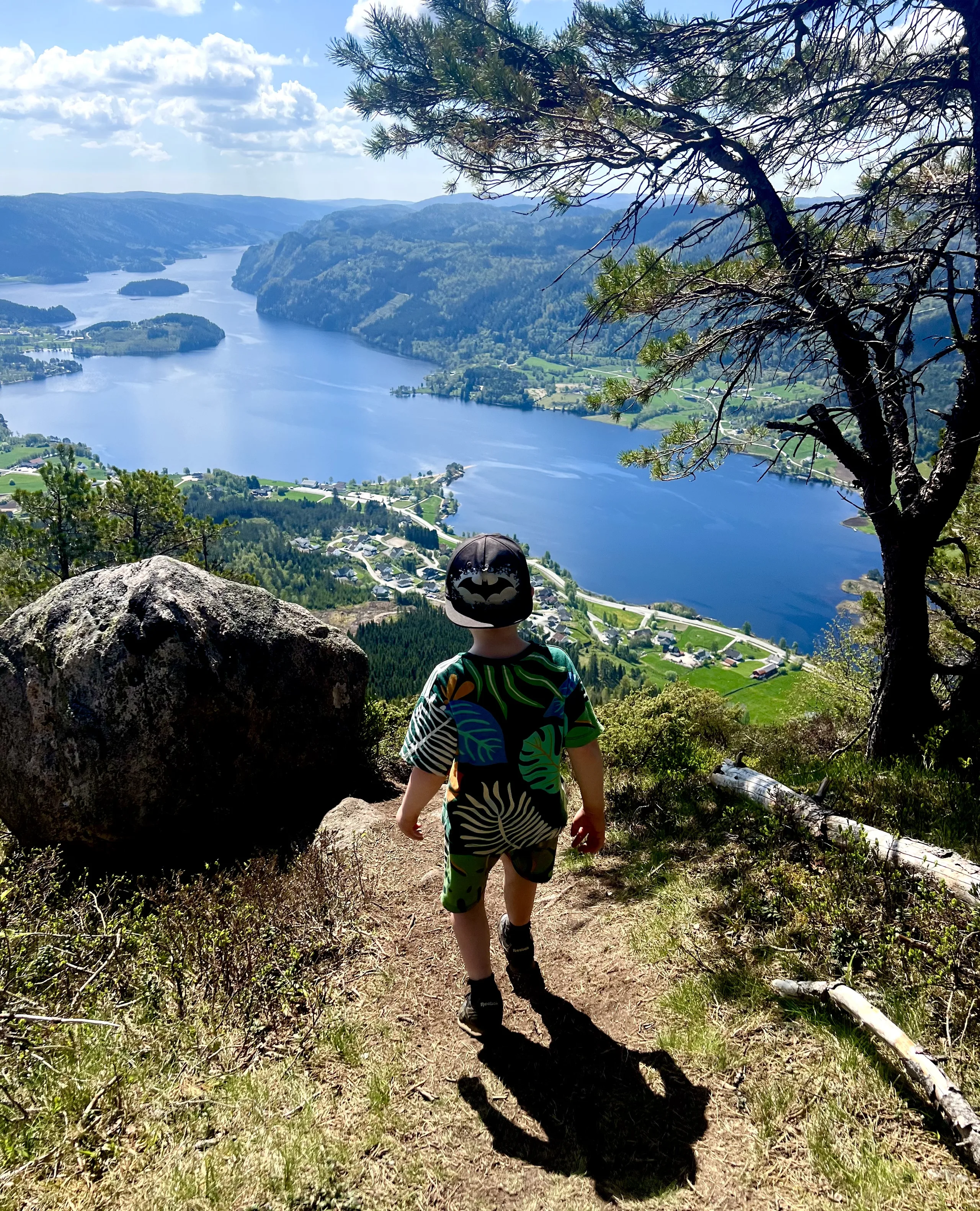 En gutt i shorts går på stien opp mot Hekkfjellet, med vannet og bygda langt der nede