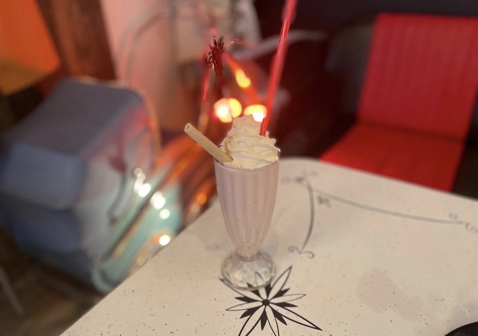 En milkshake i klassisk glass med krem og sugerør på et dinerbord