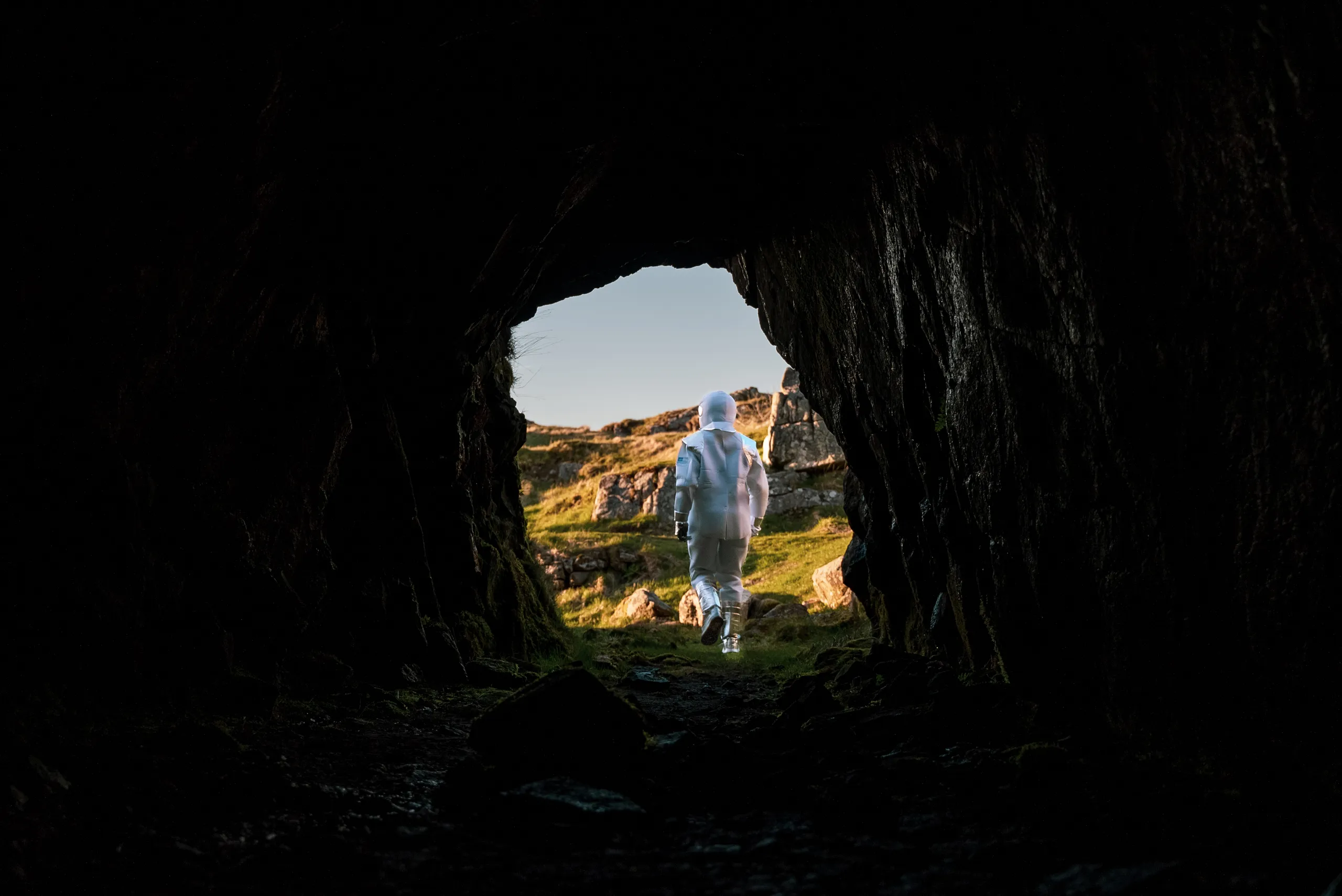 Sett innenfra en fjellgang på Hågåsen: en person i hvit drakt går ut i lyset mot et landskap av lys anortositt
