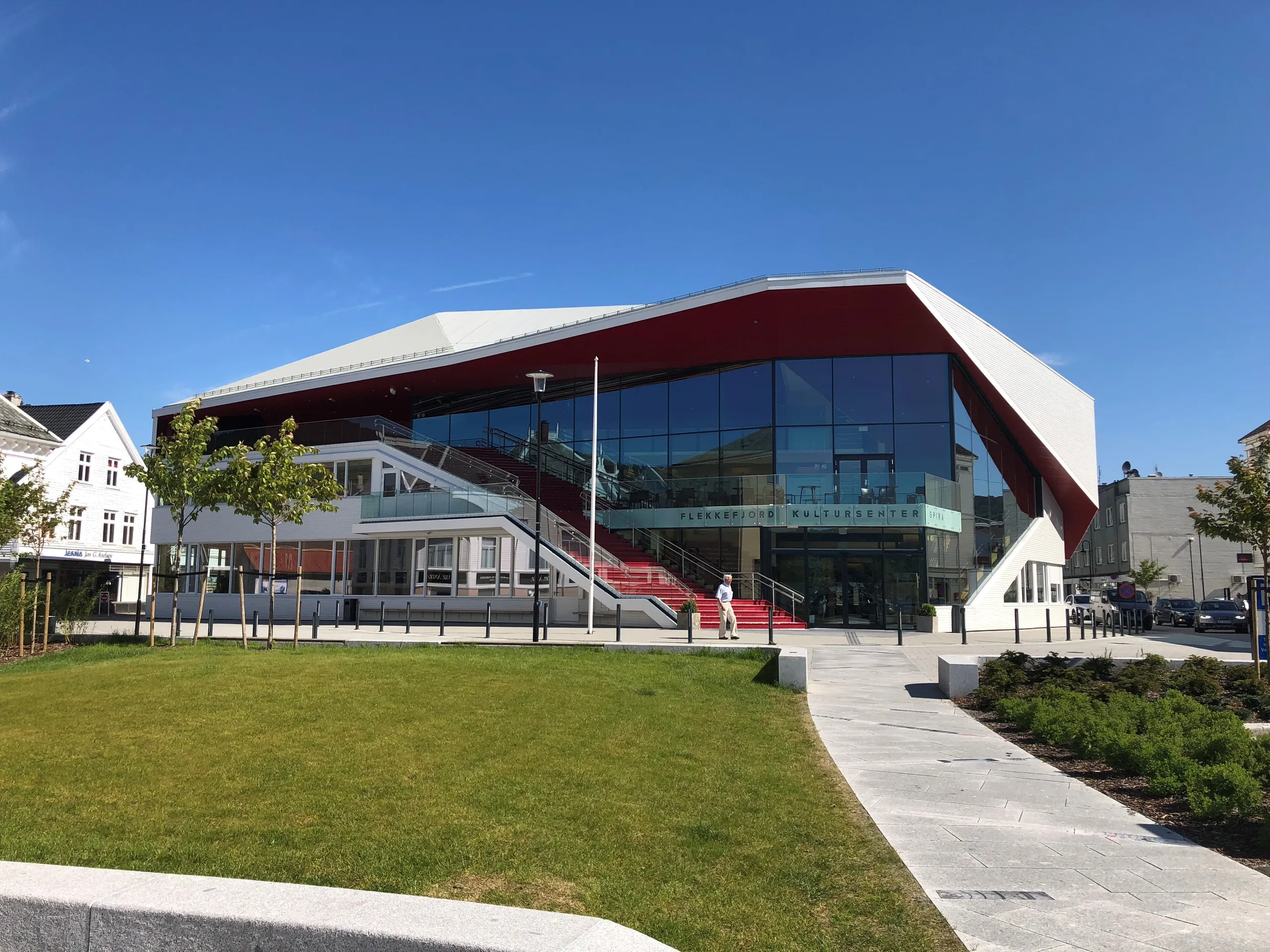 Flekkefjord kultursenter Spira: moderne bygg i glass og rødt med bred trapp og gressplen foran, hvite trehus ved siden