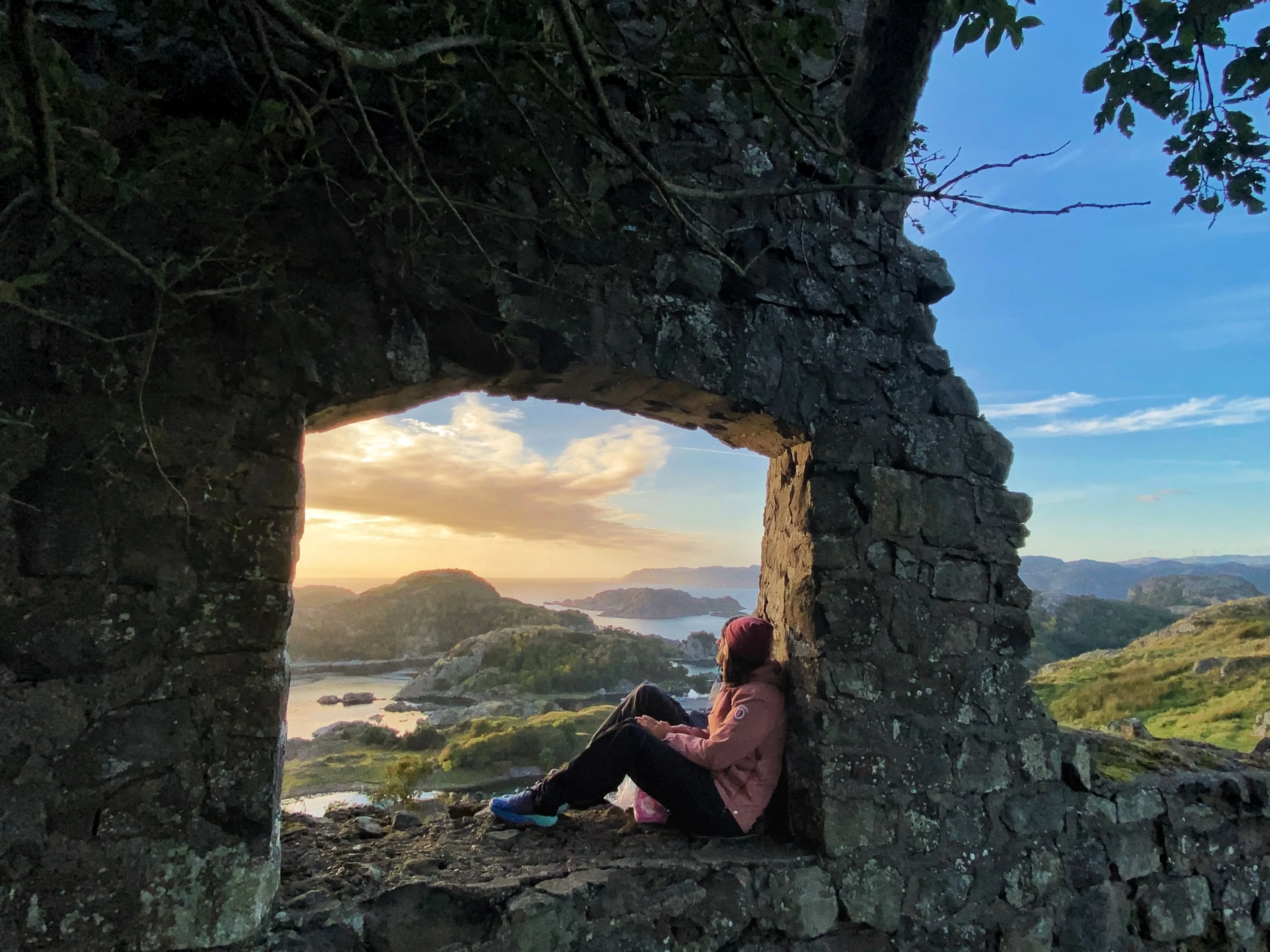 En kvinne sitter i en åpning i den gamle steinmuren på Hågåsen og ser ut over skjærgården i kveldslys