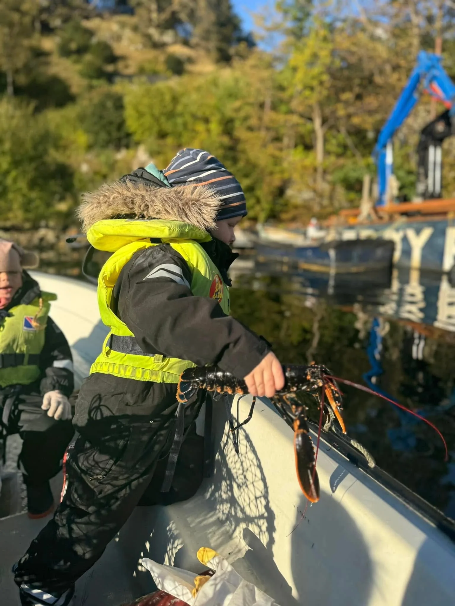 Barnehagebarn i redningsvest trekker en hummerteine over båtripa