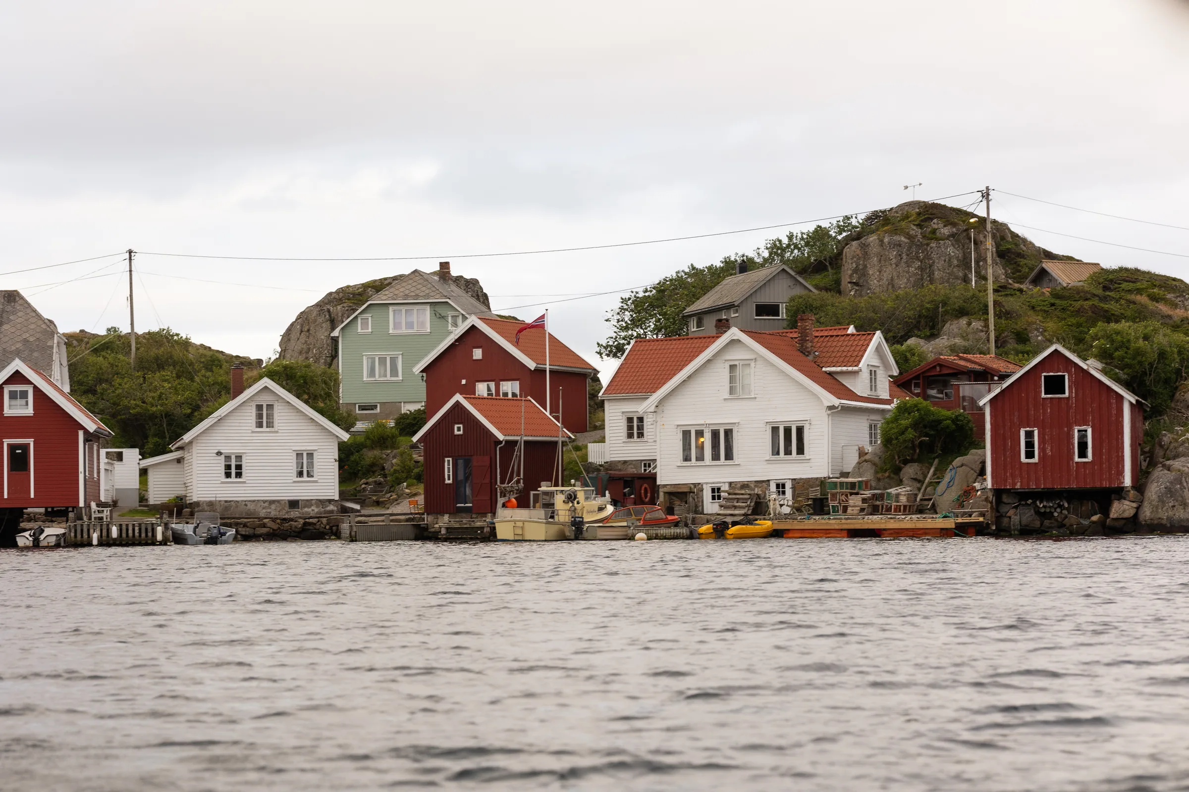 Havnemiljøet i Korshamn med hvite og røde hus, fiskebåt og teiner ved bryggene