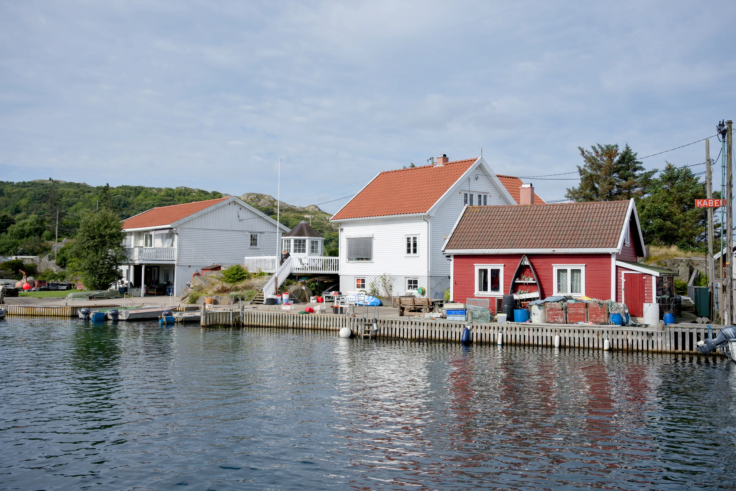 Røde og hvite hus med oransje teglsteinstak ved vannkanten, med brygge og småbåter