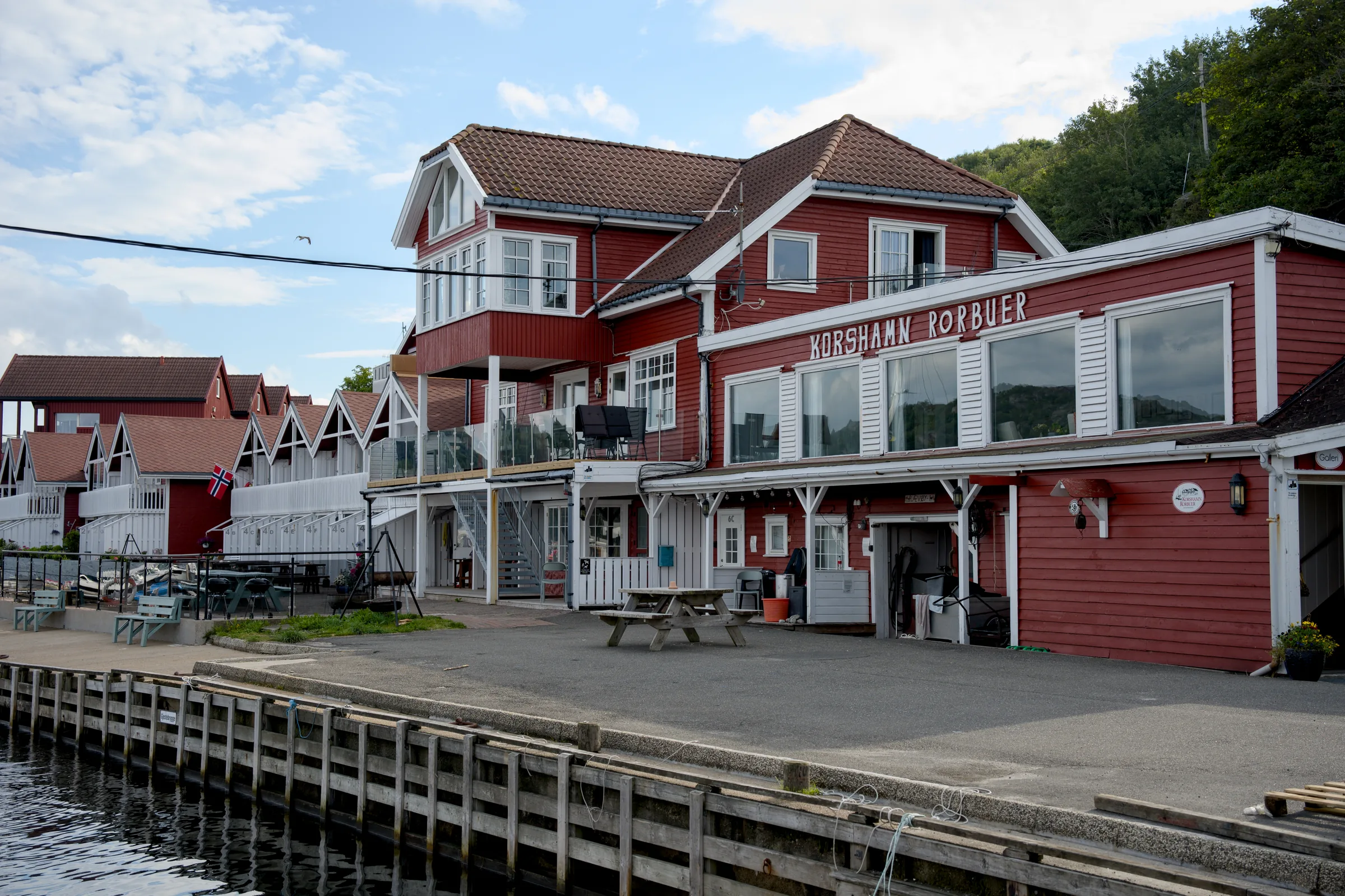 Det røde hovedbygget til Korshamn Rorbuer med balkonger og store vinduer, på kaia ved havna