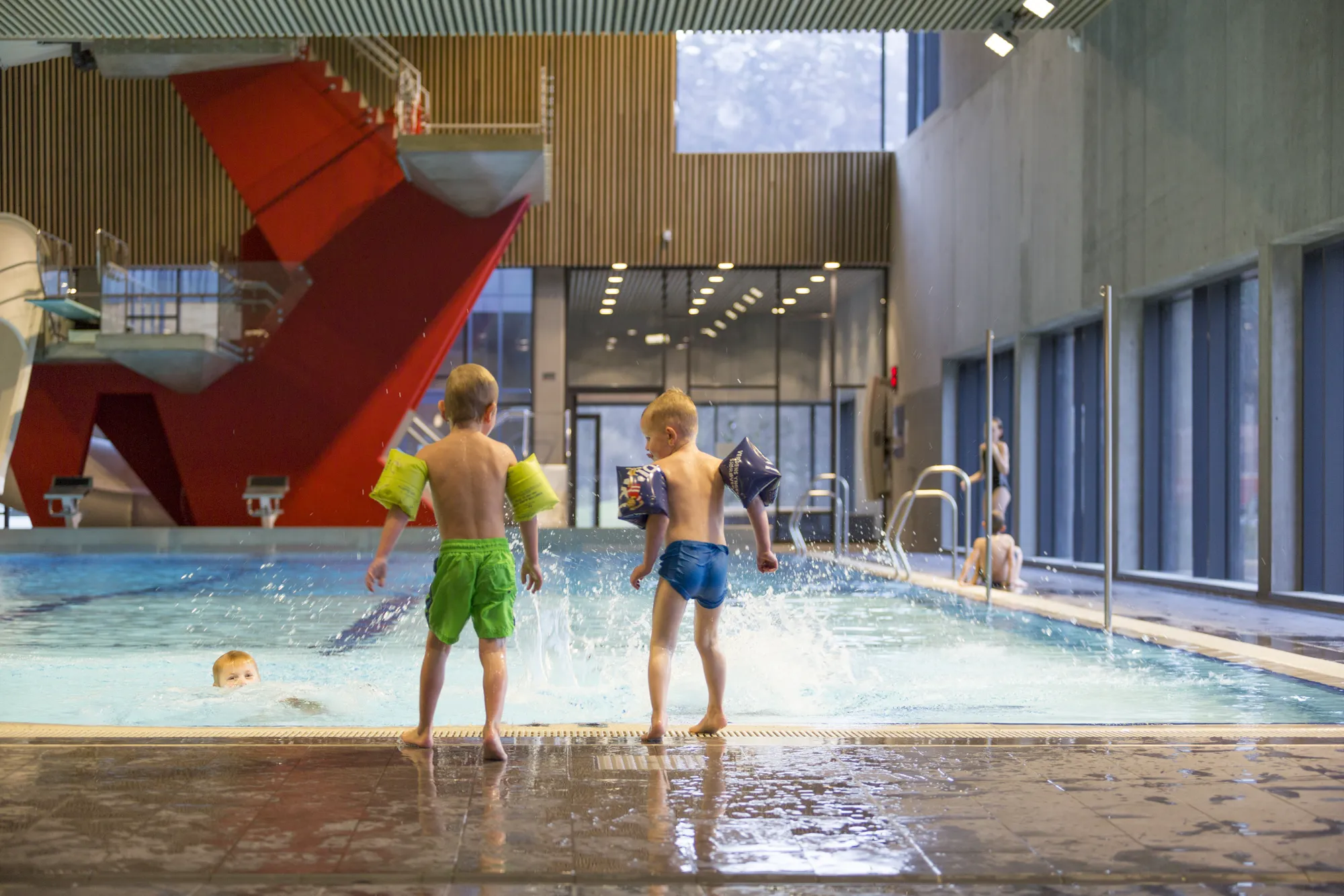 To barn med badevinger hopper i bassenget på Kvinabadet