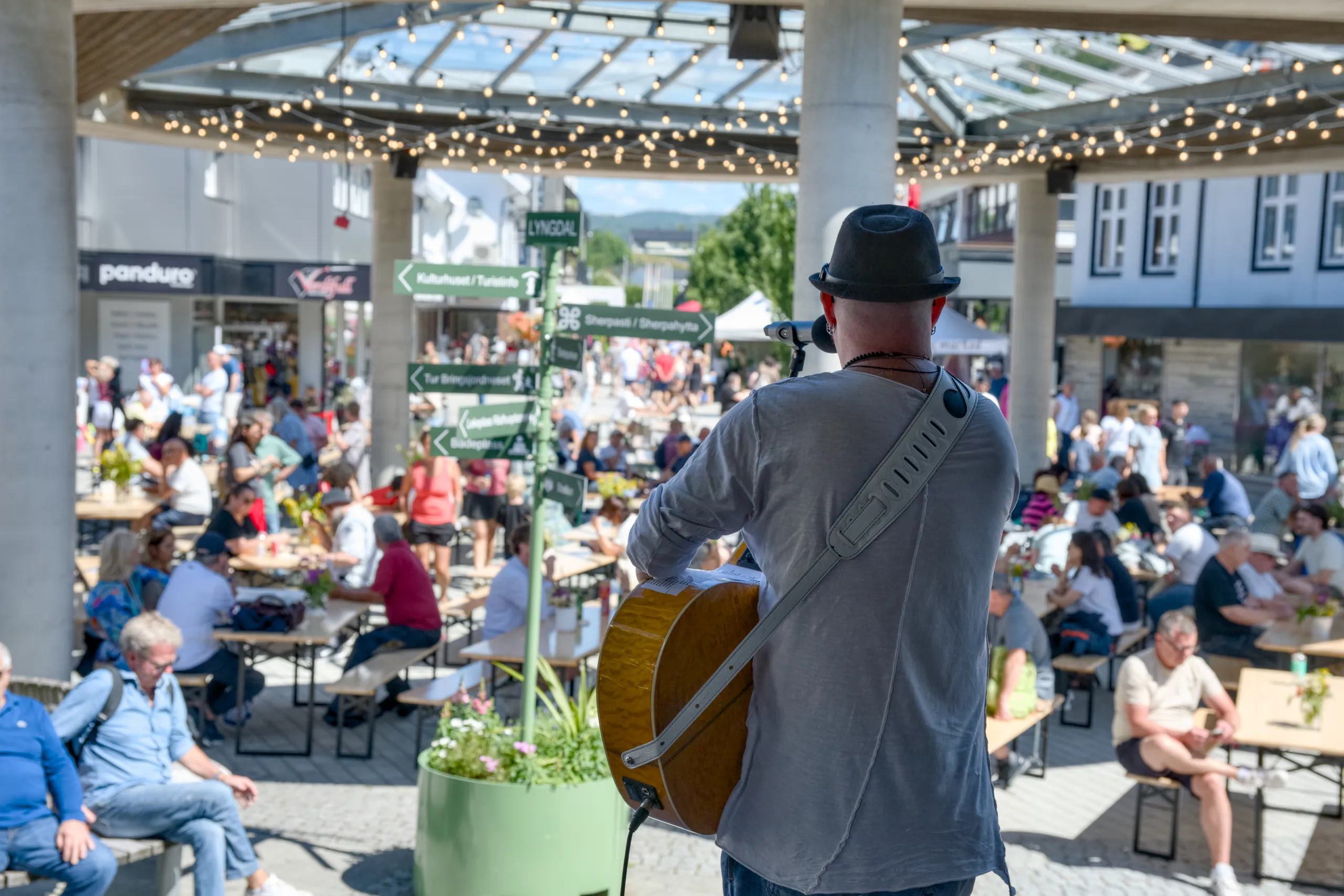Byfesten i Lyngdal sentrum: en gitarist spiller for folk ved langbord under et lysdekorert tak