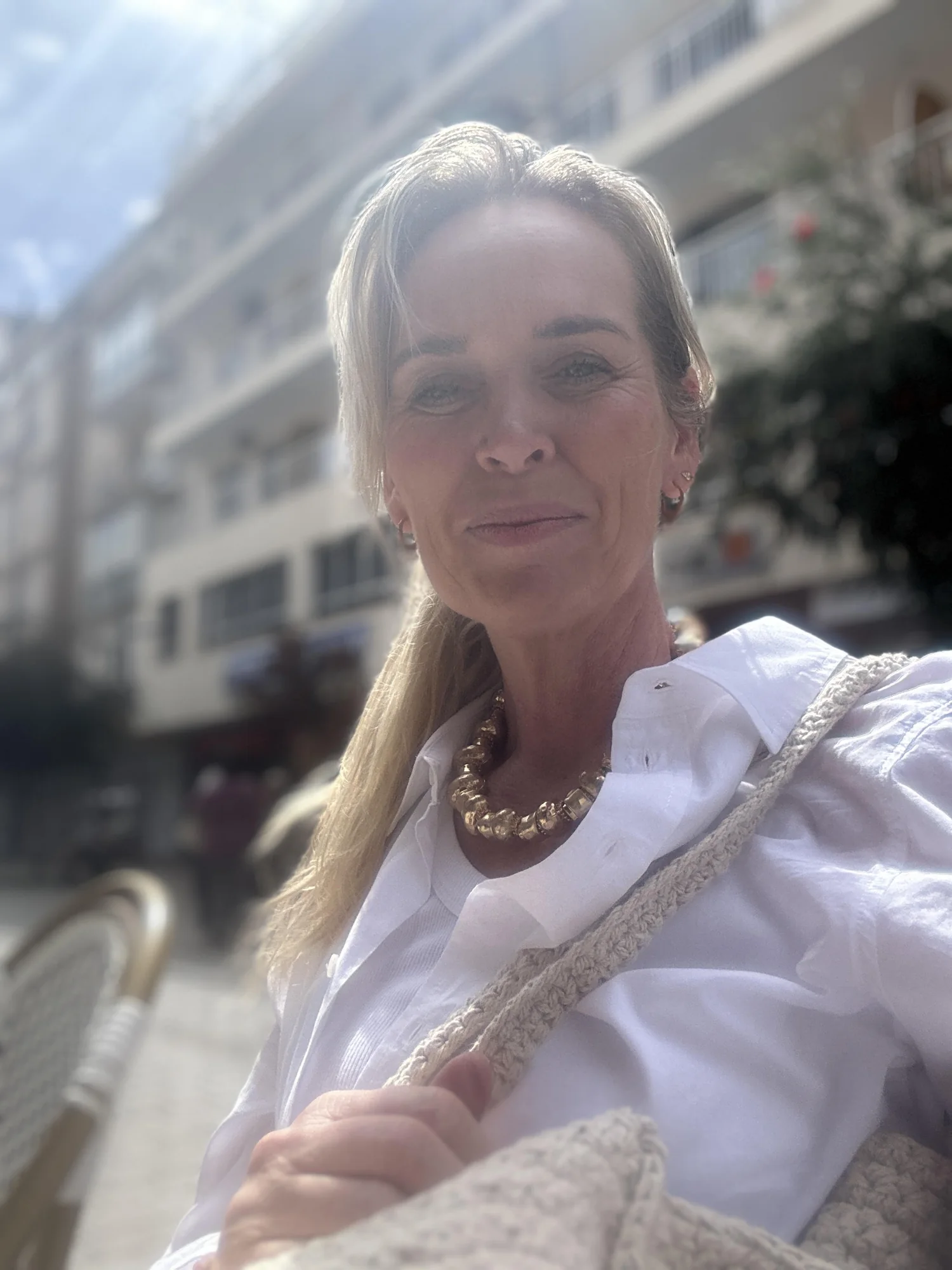 Silje Torsøe smiler på en solfylt uteservering, i hvit skjorte og perlekjede