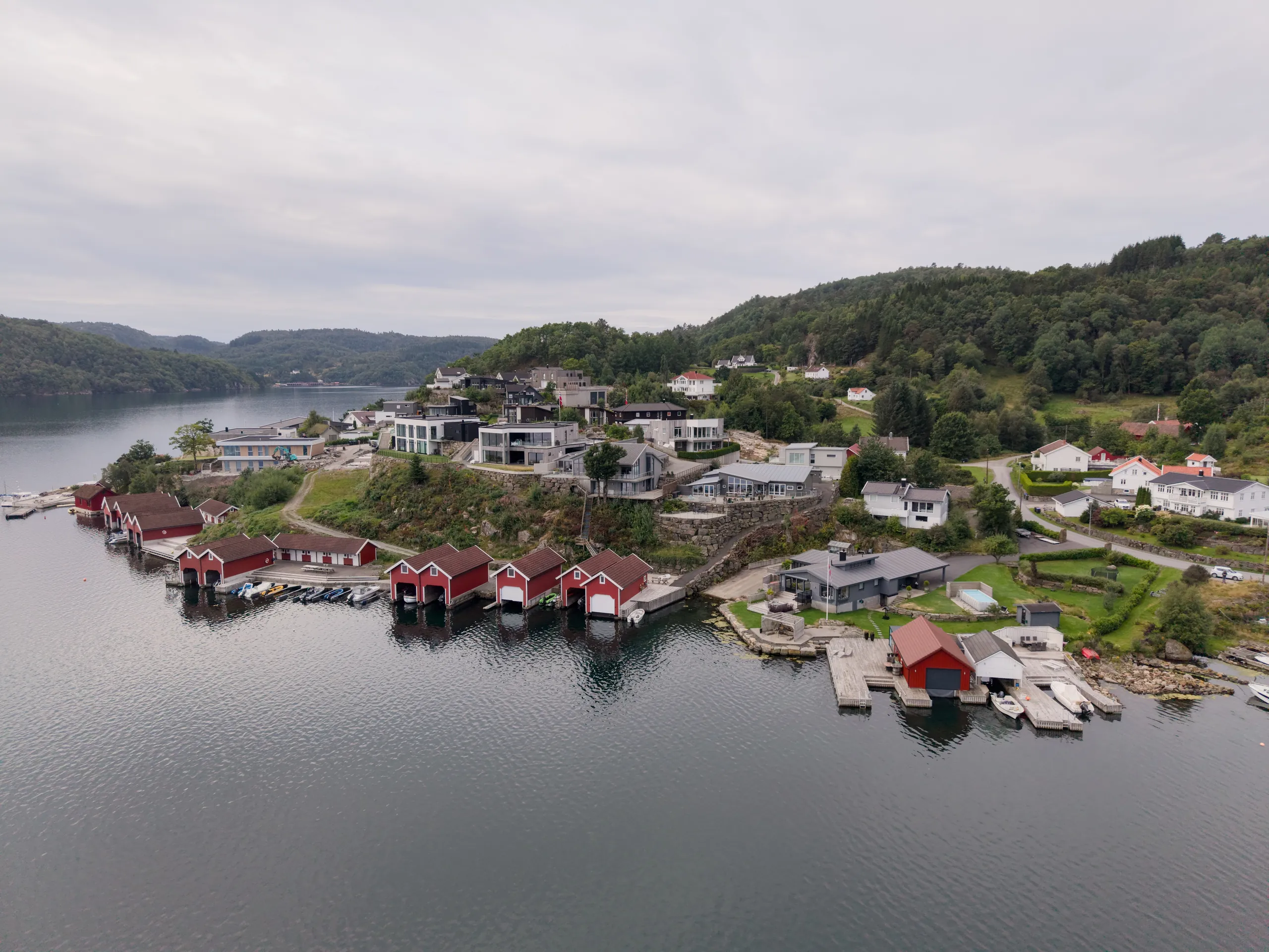 Svenevik sett fra lufta, med hus og røde naust langs fjorden og skogkledde åser bak