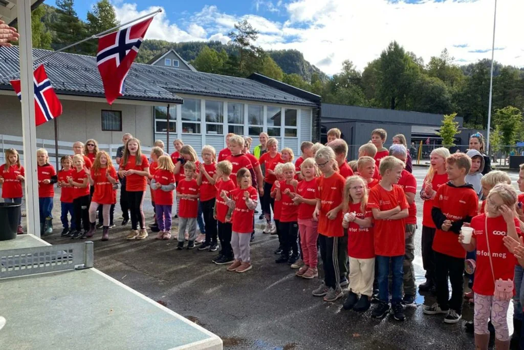 Elever i røde t-skjorter samlet foran Sira skole ved flaggstanga