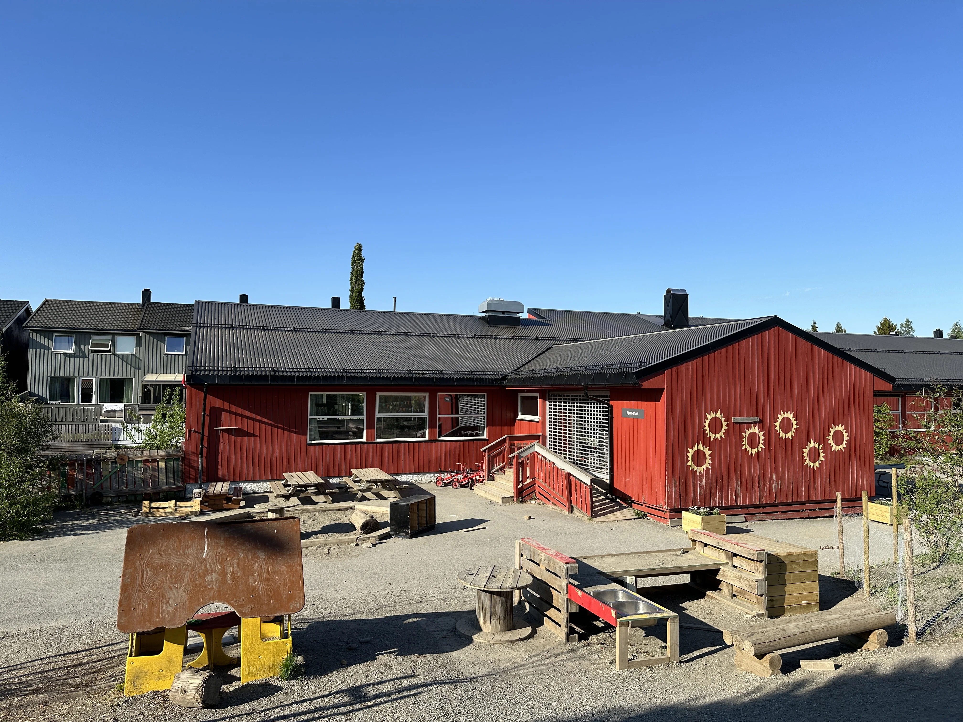 Tonstad barnehage: et rødt trehus med solsymboler på veggen og en uteplass med benker og lekeapparater