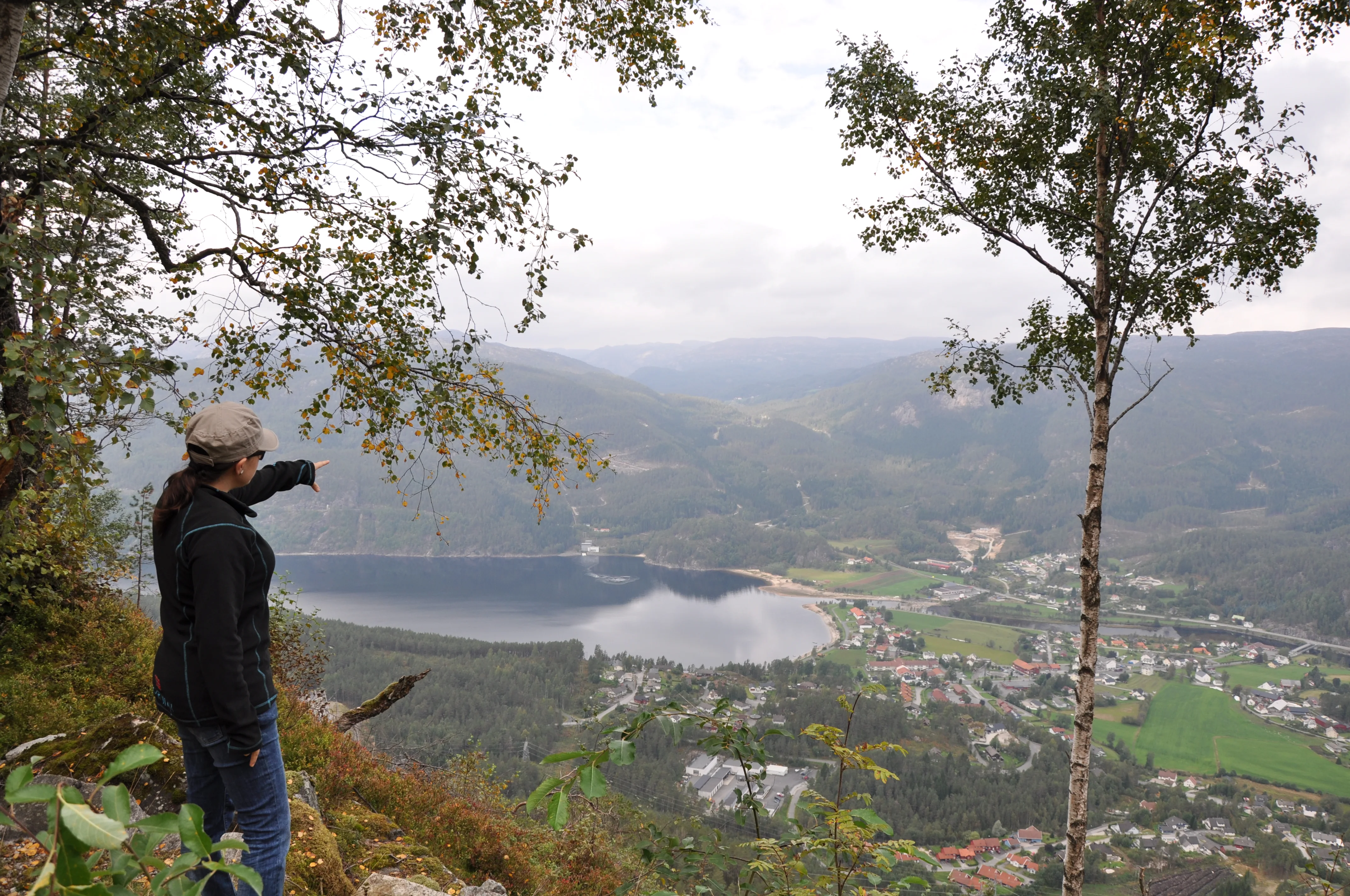 En kvinne i lia over Tonstad peker ut over bygda, Sirdalsvannet og dalen nedenfor
