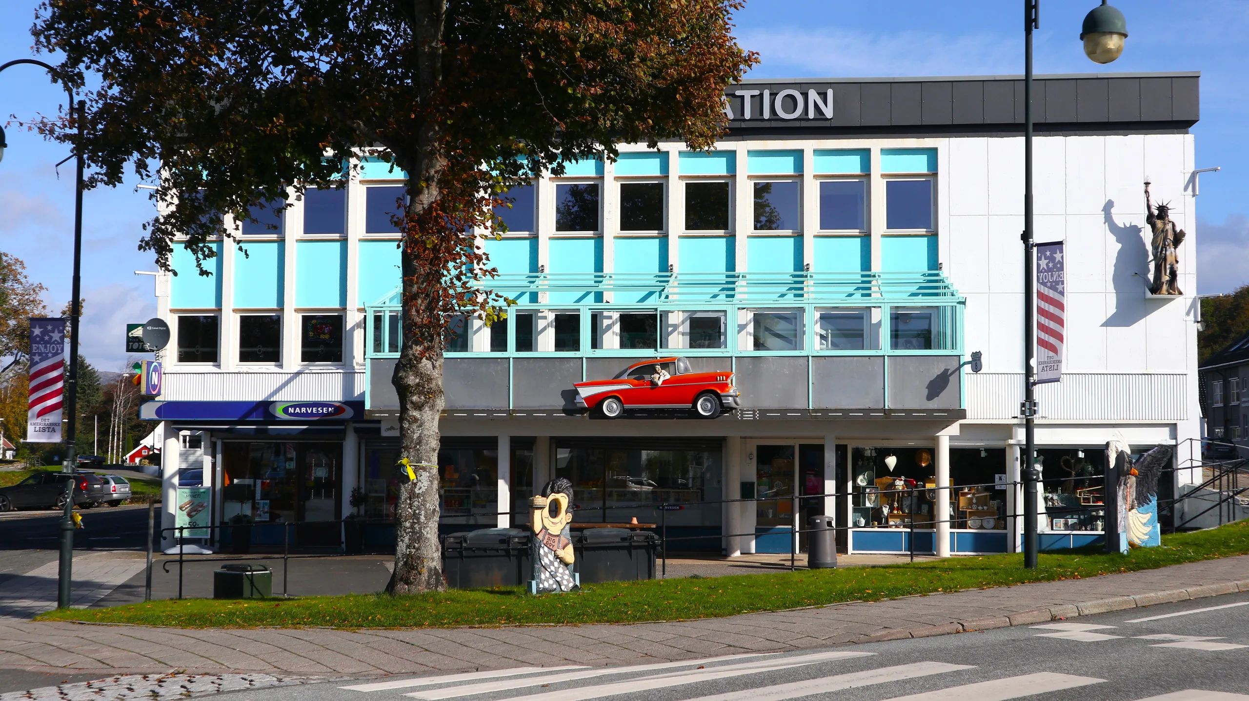 Central Station i Vanse, et turkist forretningsbygg med en rød veteranbil montert over inngangen, sett fra gata en sommerdag