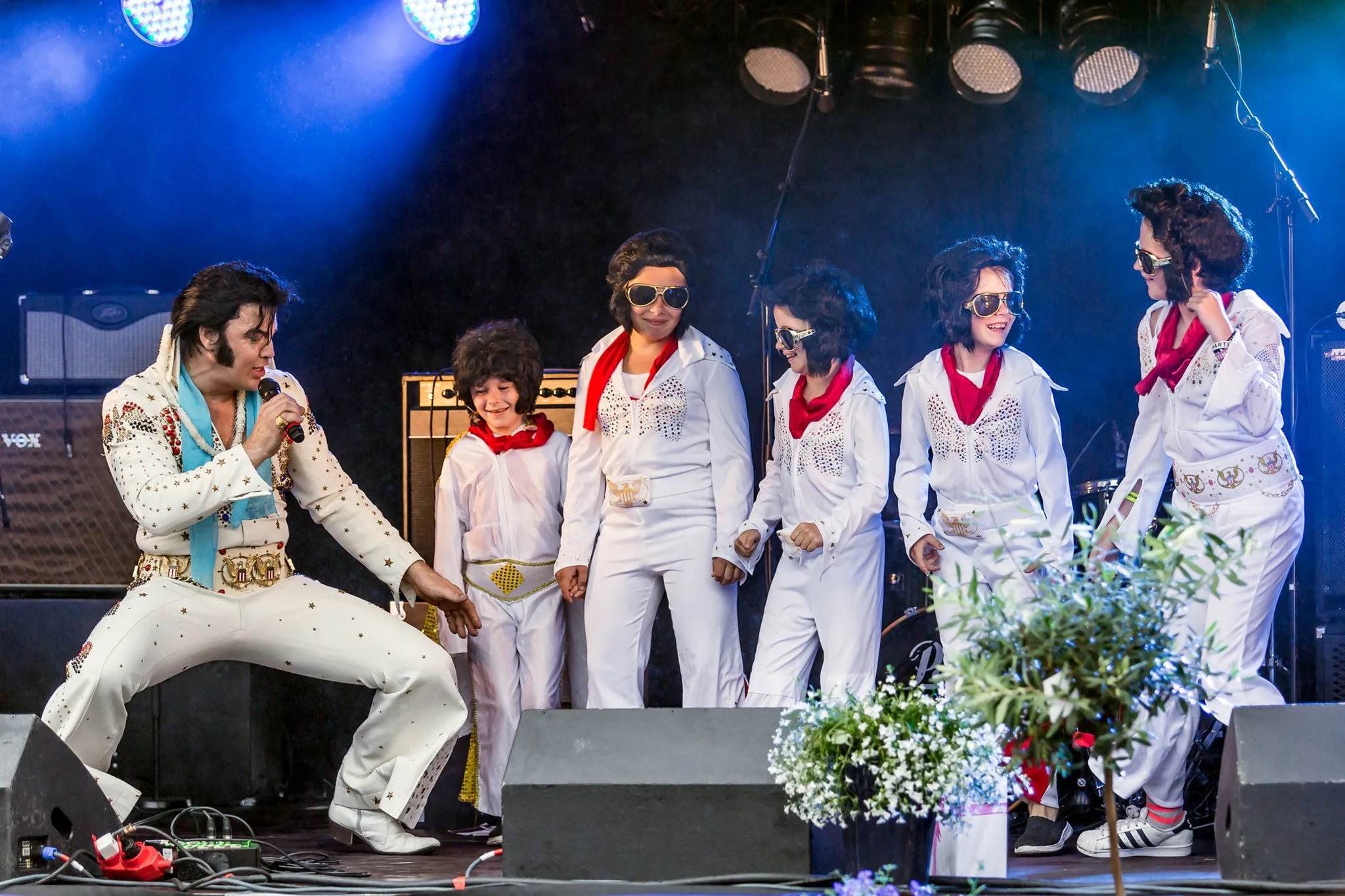 Fem Elvis-artister i hvite dresser på scenen, den ene med mikrofon