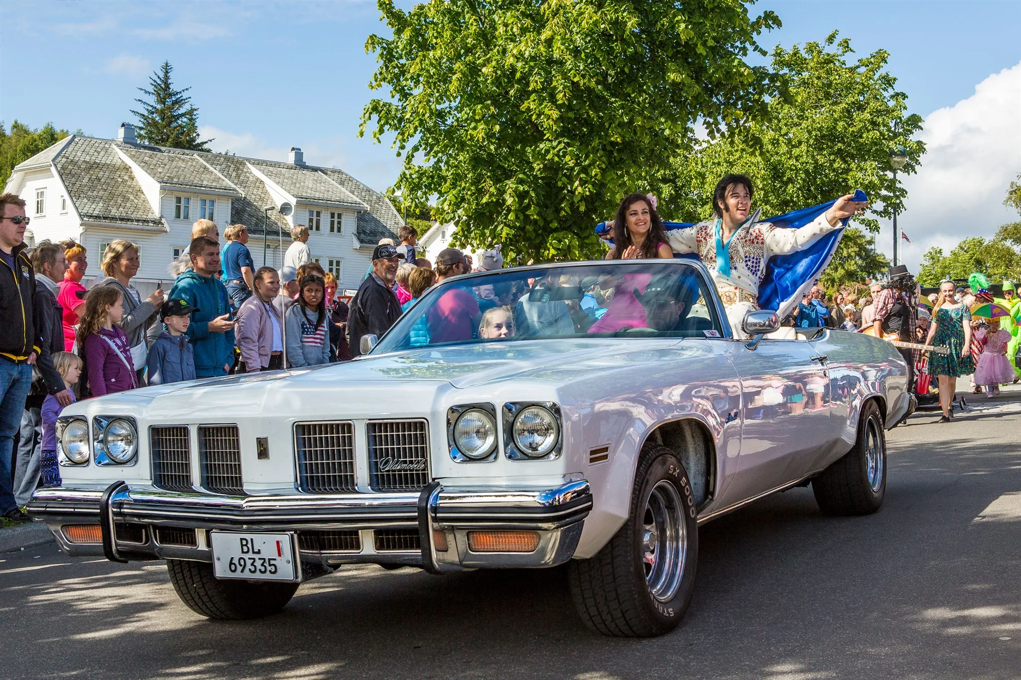 En hvit amerikansk kabriolet med Elvis-artist i baksetet kjører gjennom folkemengden i gateparaden