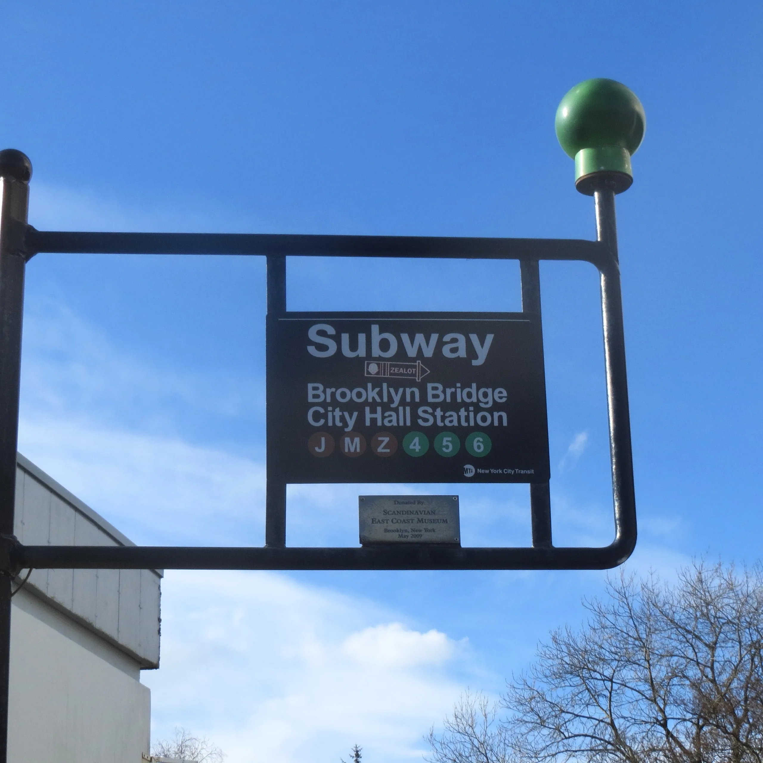 Et Subway-skilt for Brooklyn Bridge – City Hall Station på en stolpe i Vanse, mot blå himmel