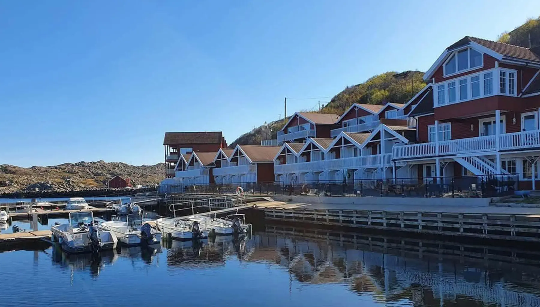 Rorbuer i rødt og hvitt langs en båthavn i Korshamn, med fjell i bakgrunnen