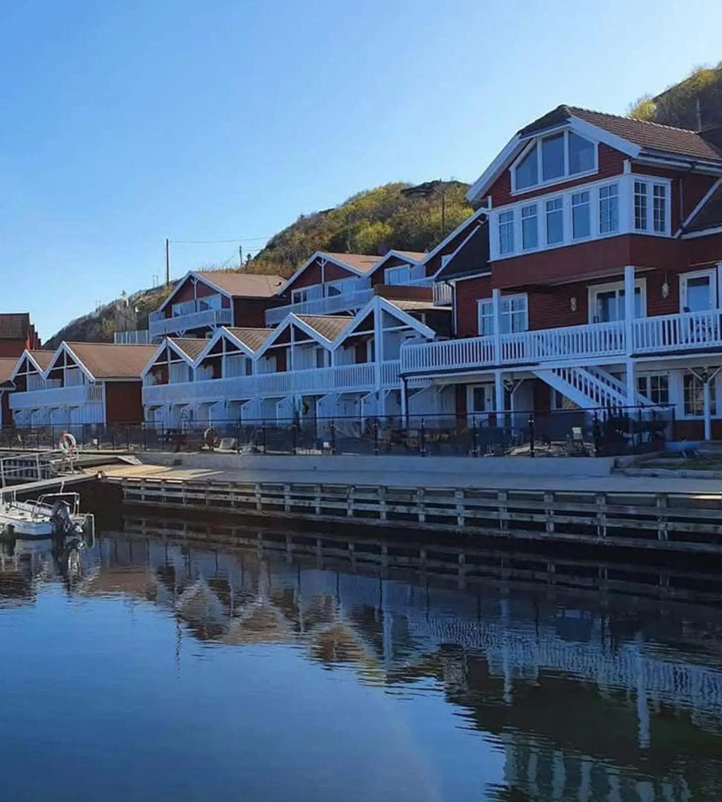 Rorbuer i rødt og hvitt langs en båthavn i Korshamn, med fjell i bakgrunnen