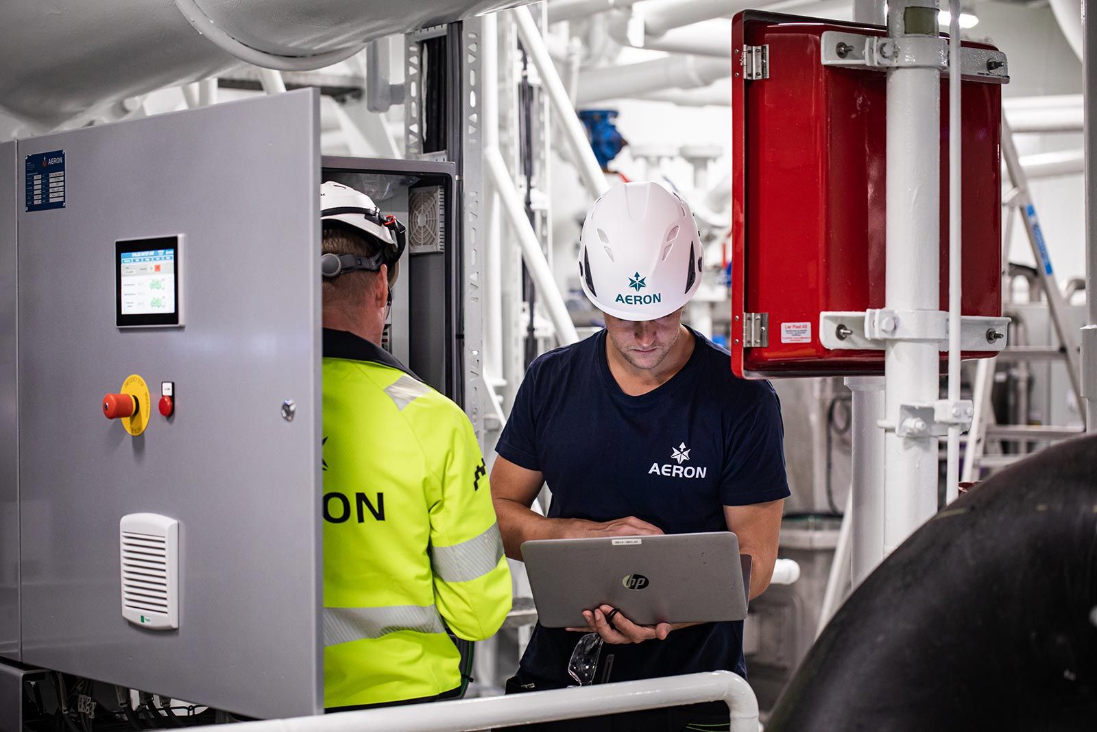 To ansatte fra Aeron i arbeid med teknisk anlegg, den ene med laptop