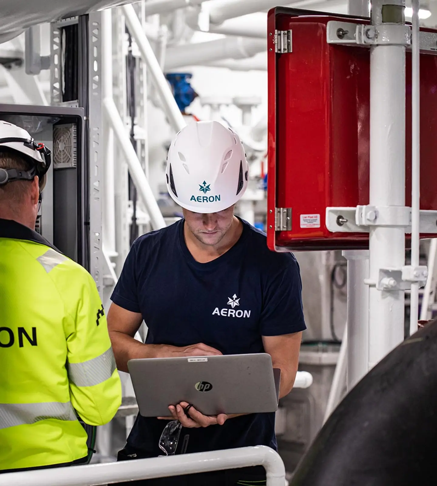To ansatte fra Aeron i arbeid med teknisk anlegg, den ene med laptop