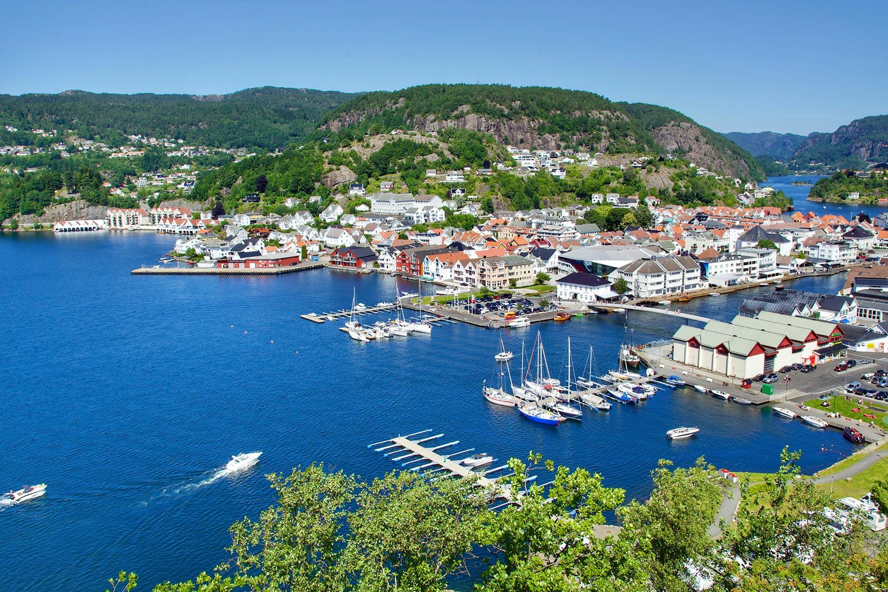 Flyfoto av Flekkefjord sentrum med fjorden, båthavn og bebyggelse omkranset av grønne åser