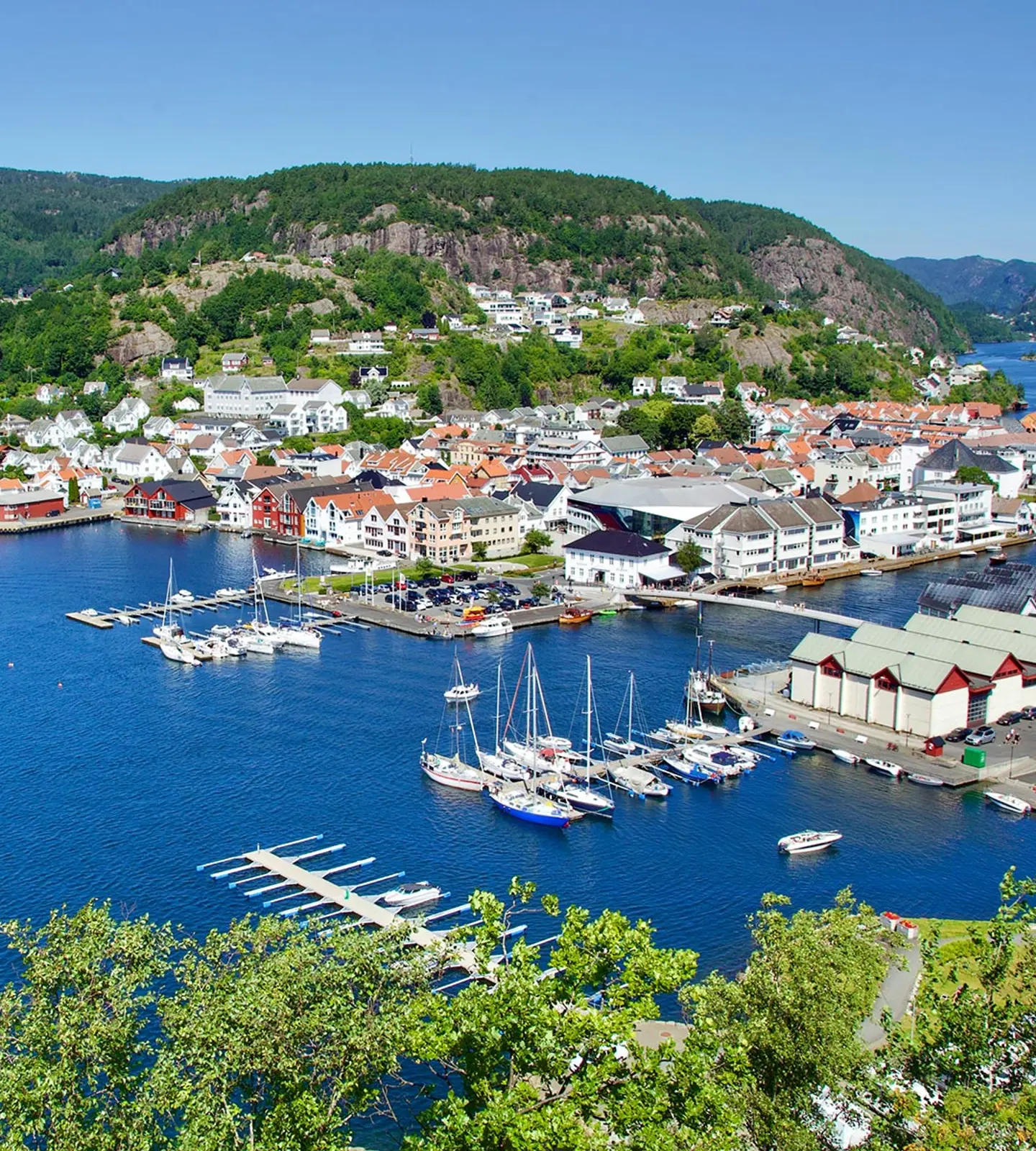 Flyfoto av Flekkefjord sentrum med fjorden, båthavn og bebyggelse omkranset av grønne åser