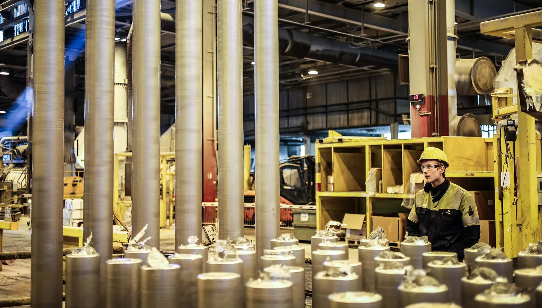 Produksjonshallen på Alcoa Lista med lange aluminiumsstenger og en ansatt i vernutstyr