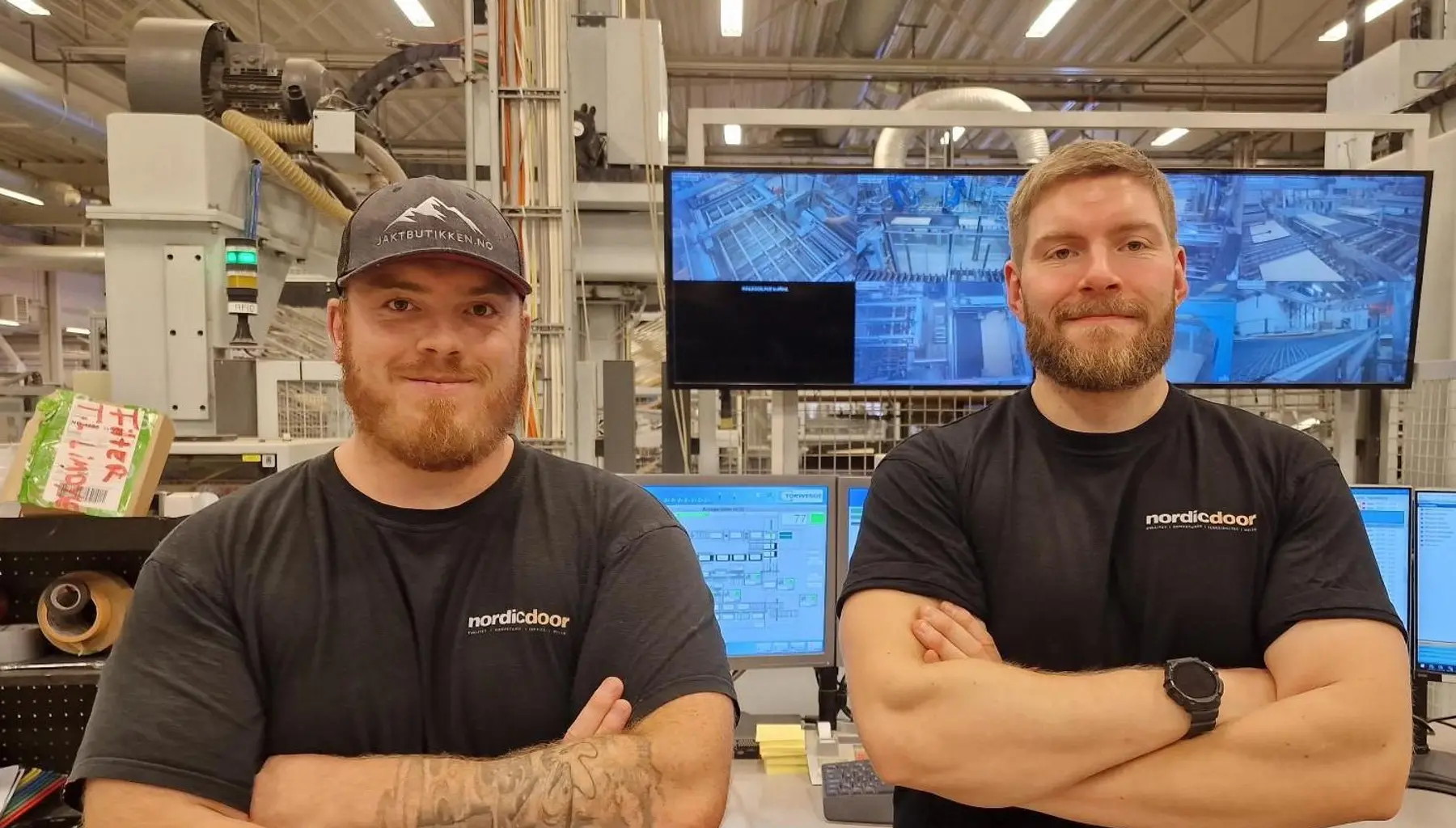 To ansatte i produksjonshallen hos Nordic Door foran skjermer som viser produksjonslinjen