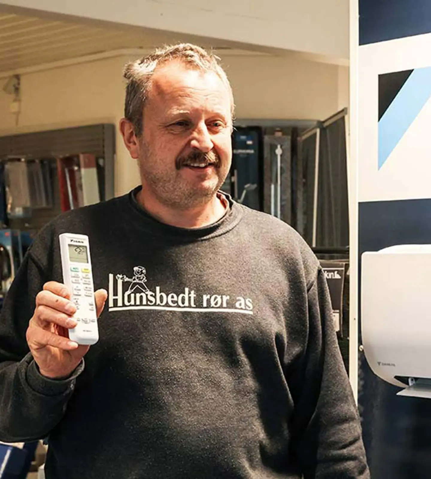Rørlegger fra Hunsbedt Rør viser fram en varmepumpestyring ved siden av en Daikin-utstilling i butikken