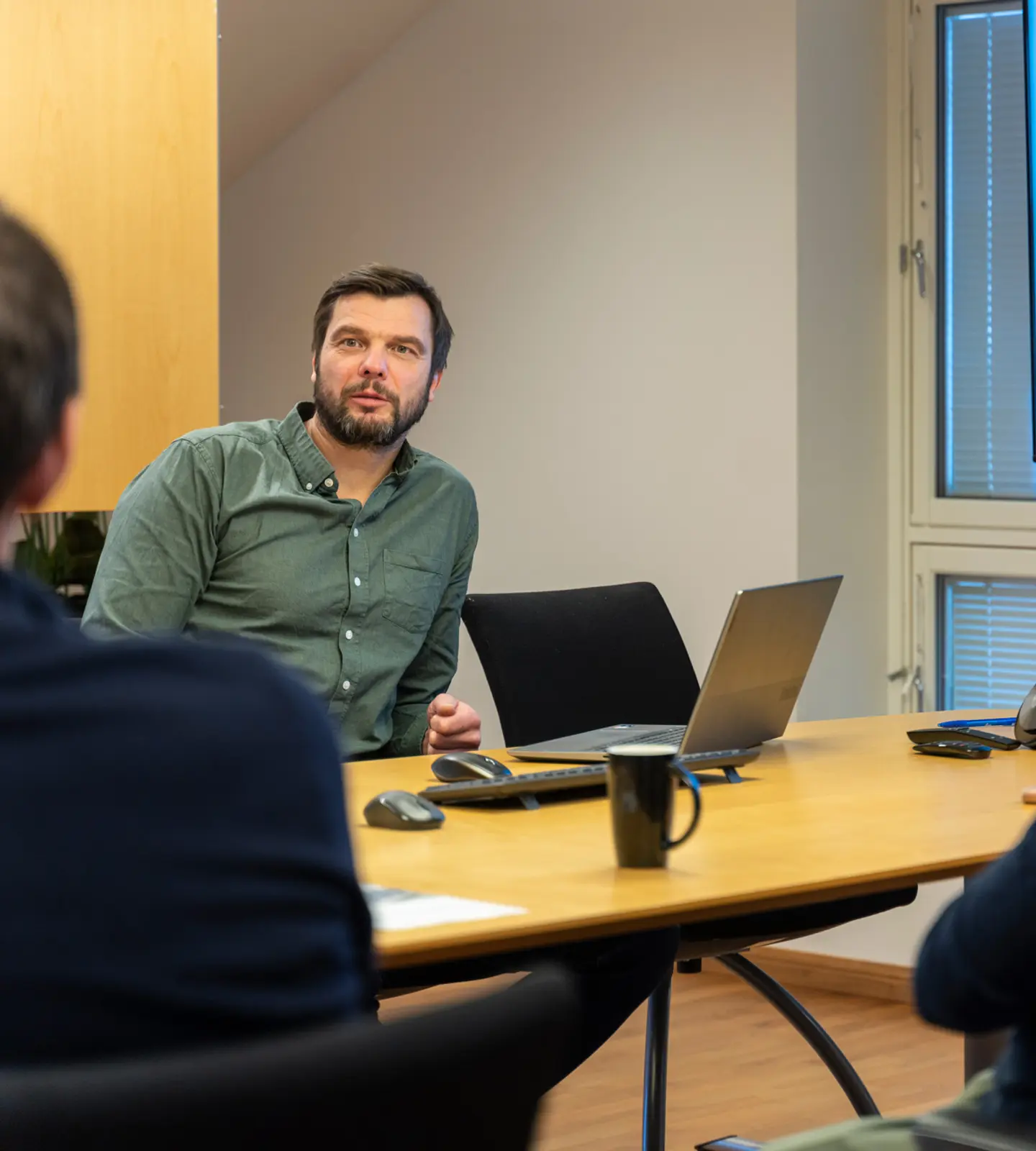 Ansatte i AMS i møte rundt et bord, med produksjonsdata vist på skjerm i bakgrunnen