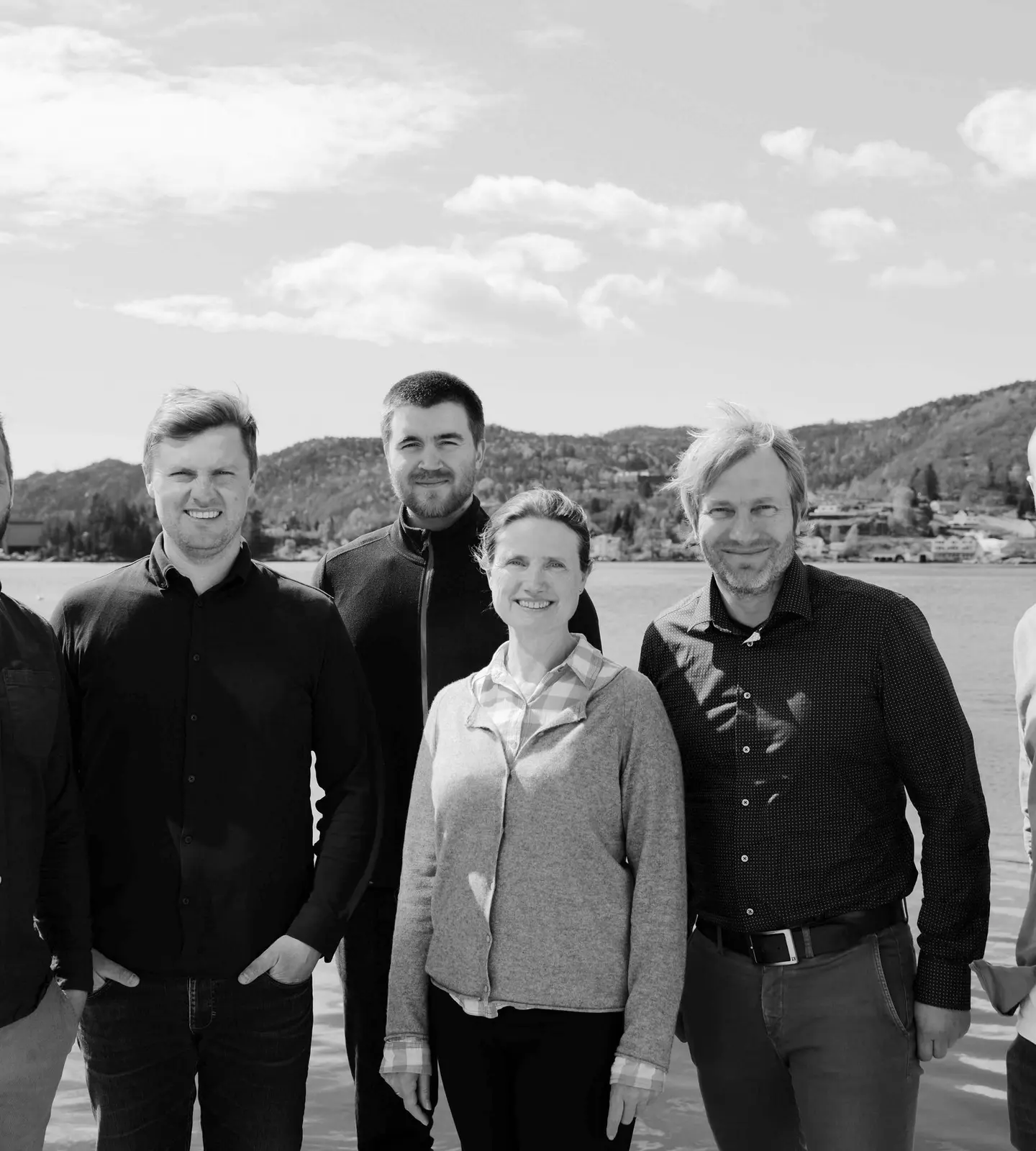 Gruppebilde av de seks ansatte i Pilar Byggrådgivning, stående samlet ved sjøen i Flekkefjord