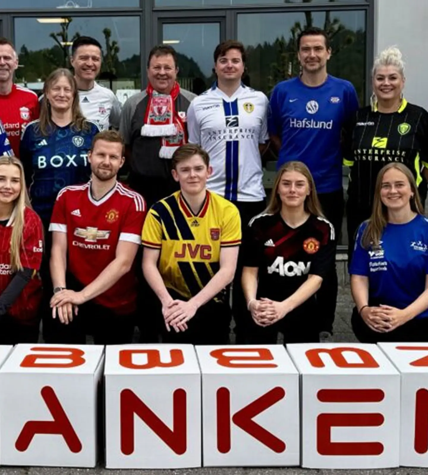 Ansatte i Kvinesdal Sparebank samlet utenfor banken i fotballdrakter, med store bokstavkubber som staver BANKEN foran seg