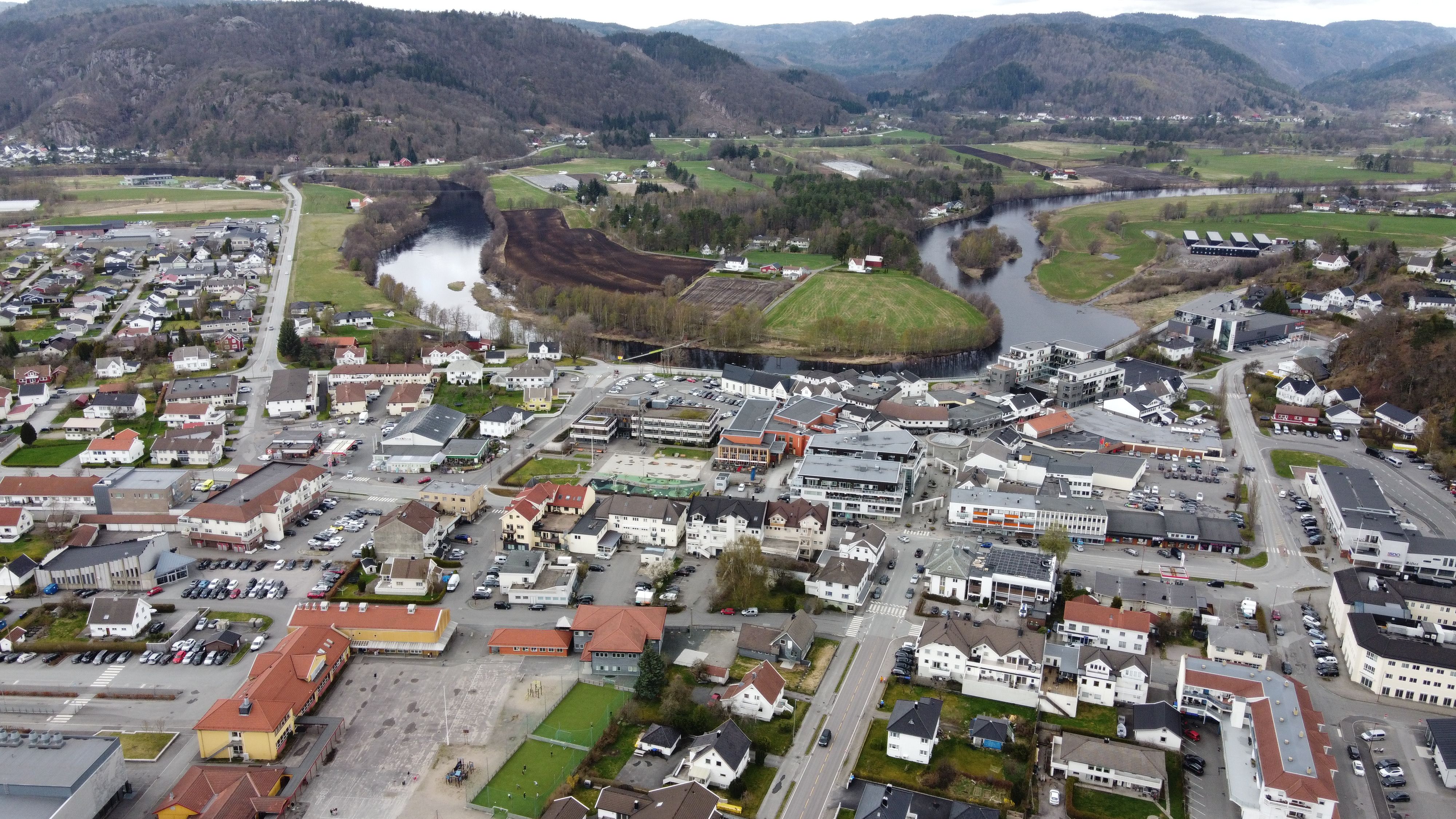 Aerial drone view of Lyngdal town center, with the river running through the settlement and hills in the background
