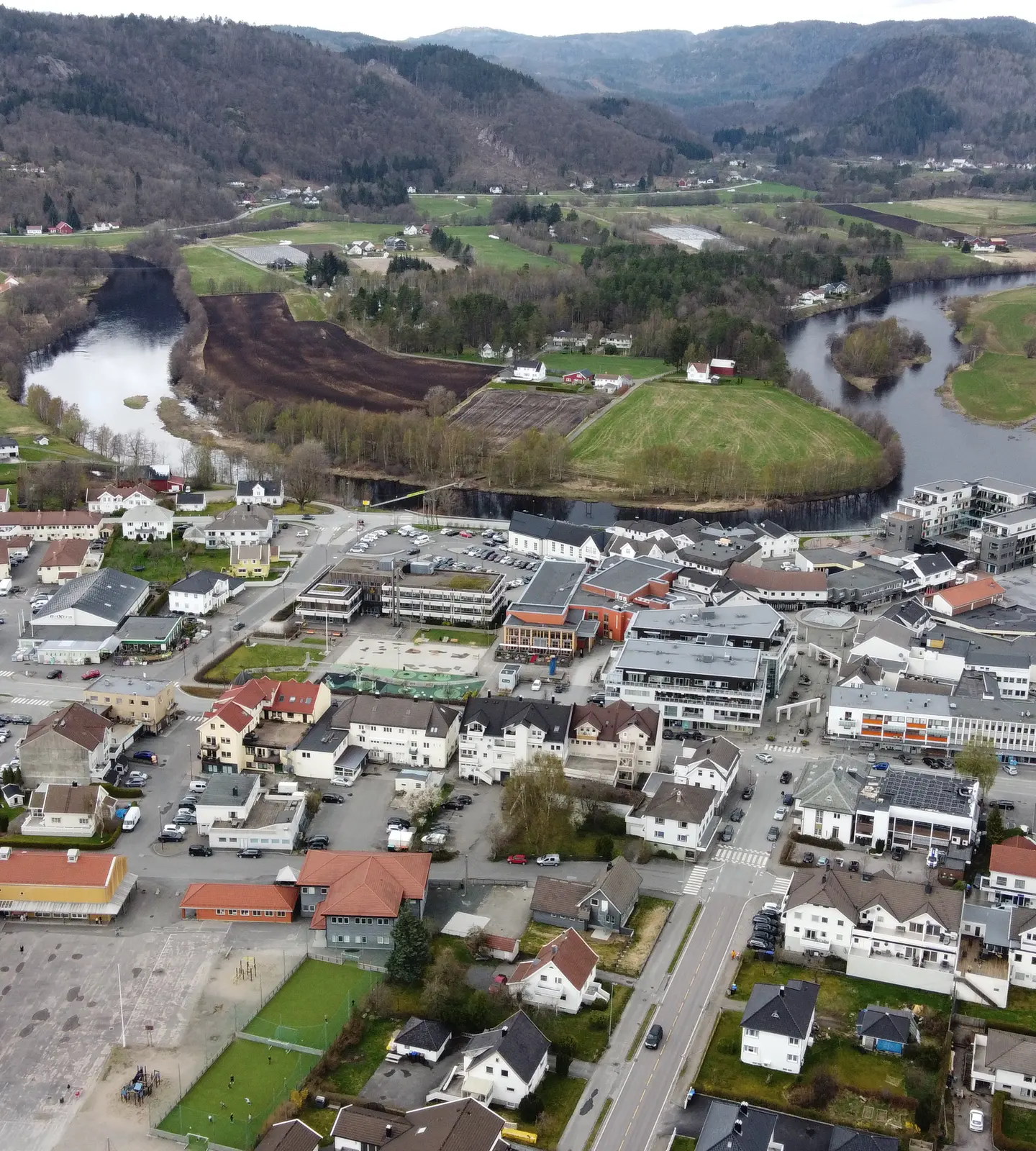 Aerial drone view of Lyngdal town center, with the river running through the settlement and hills in the background