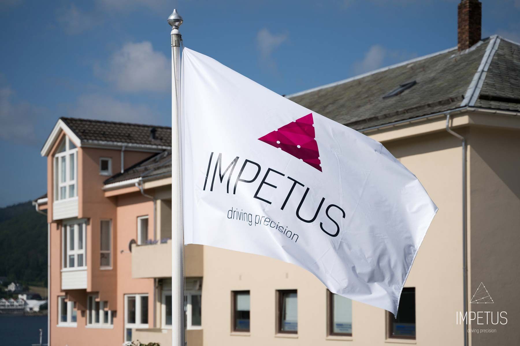 Hvitt IMPETUS-flagg med logoen «driving precision» vaier foran kontorbygningen i Flekkefjord