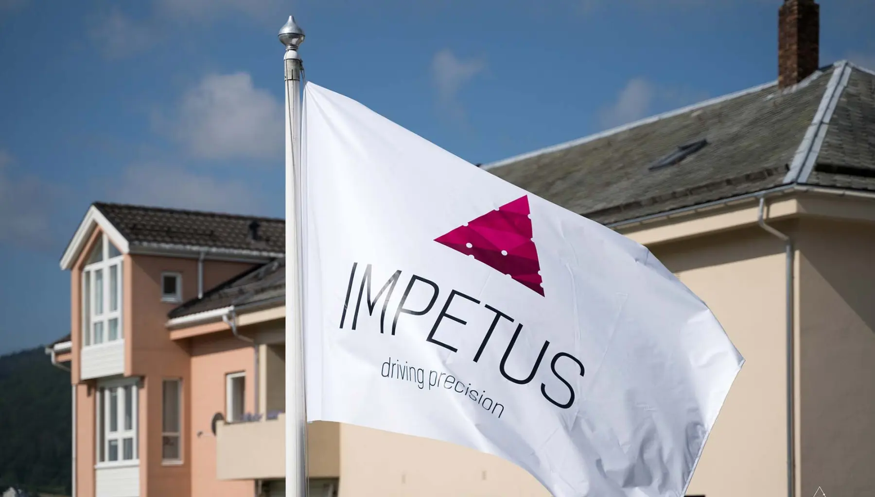 IMPETUS-flagget vaier i vinden foran kontorbygningen ved sjøen i Flekkefjord